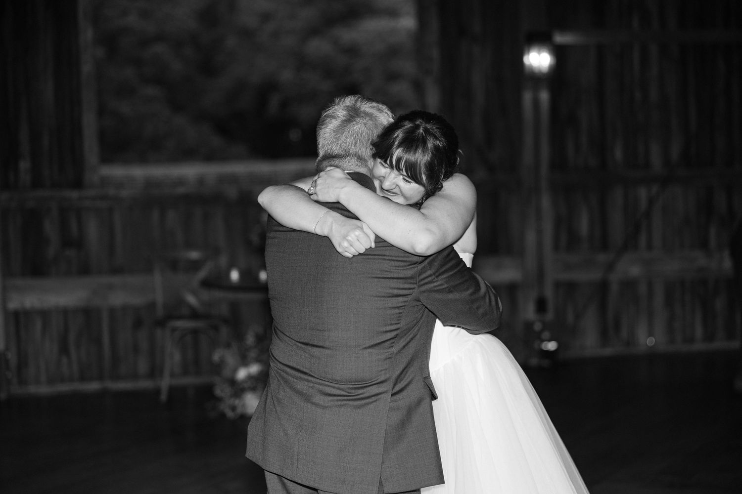 Black and white photo of a bride embracing an older man in a suit during an emotional father-daughter wedding dance.