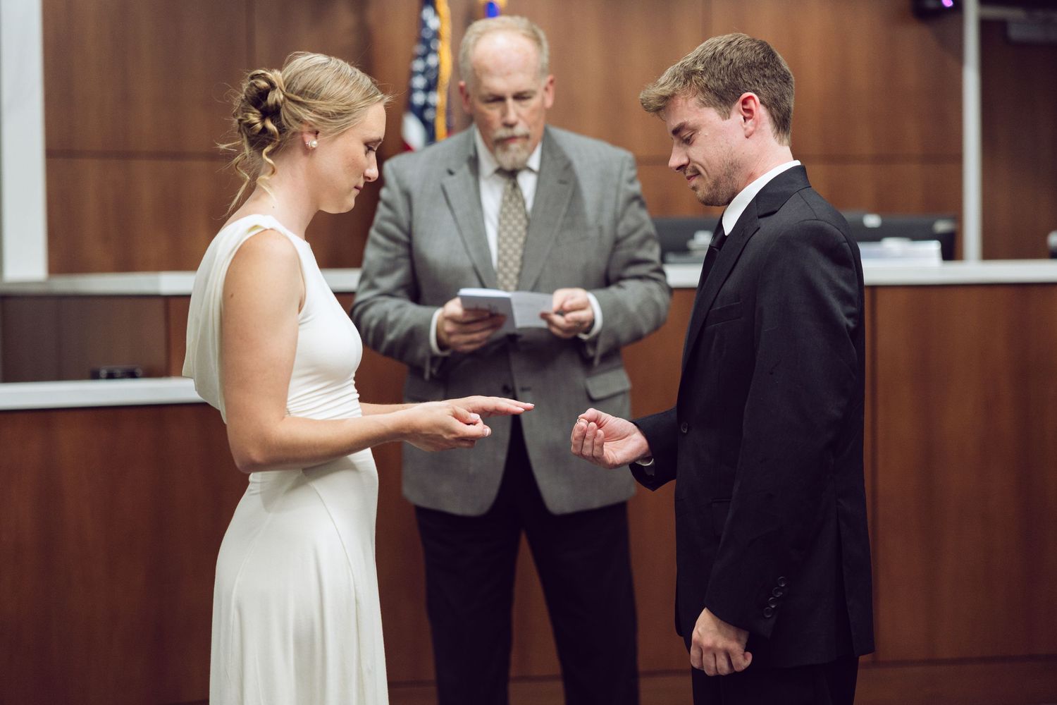 Bride and groom exchange rings as the officiant reads from a paper during their intimate courthouse wedding ceremony.