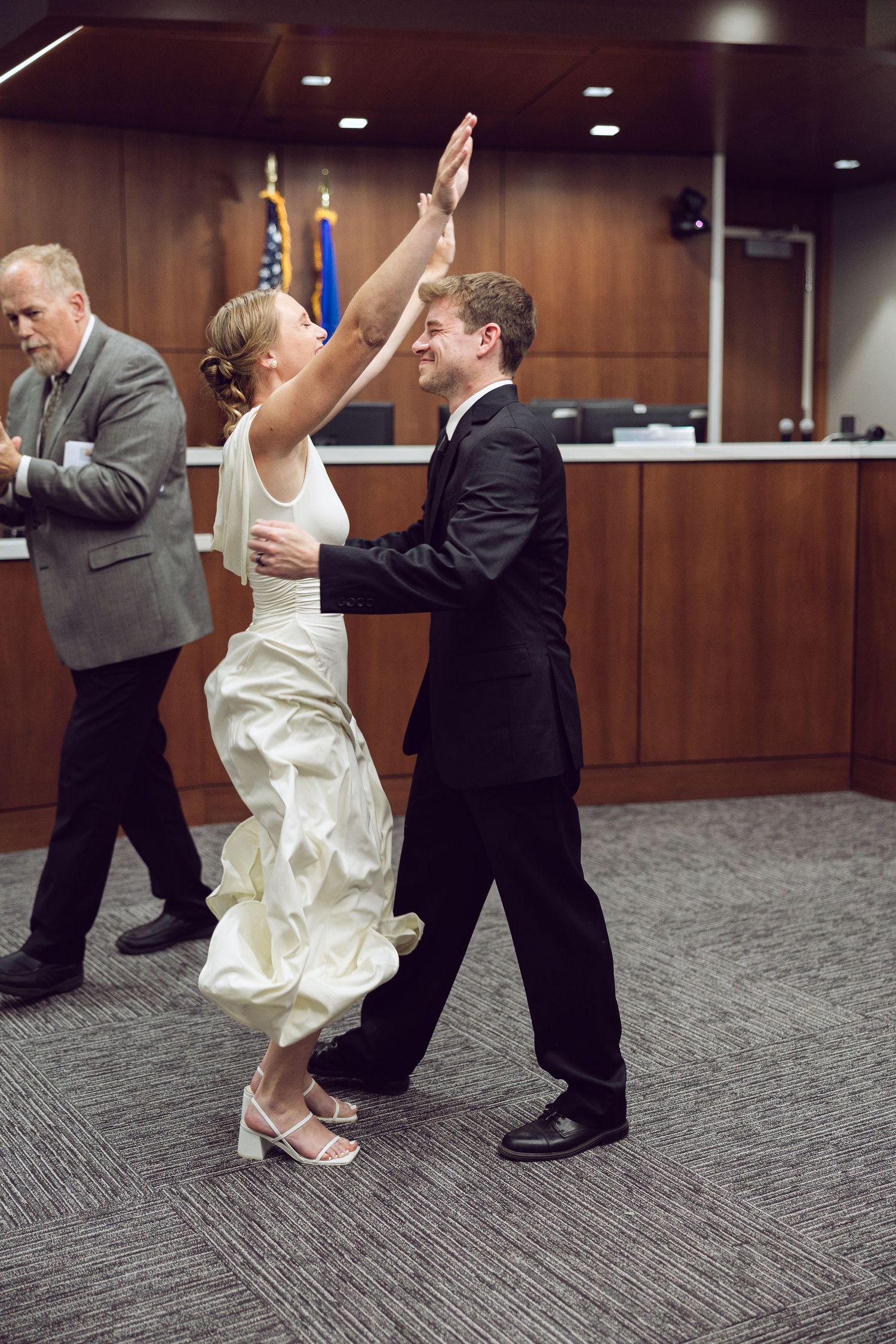 Groom twirls the bride in her white wedding dress as they dance happily in a courthouse after their ceremony.