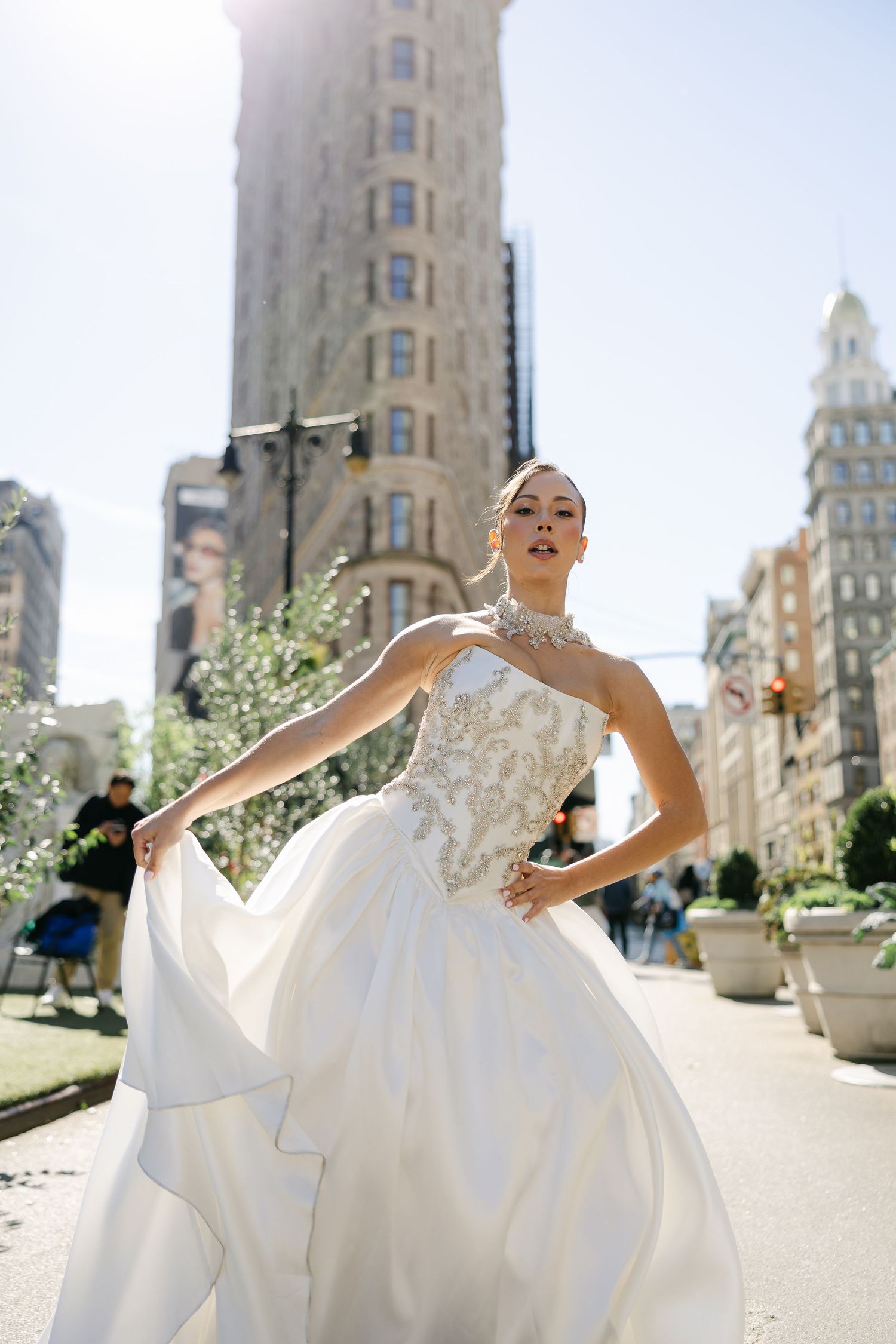 Bride in a flowing white ball gown with embellished bodice twirls on a Manhattan street with the Flatiron Building behind.