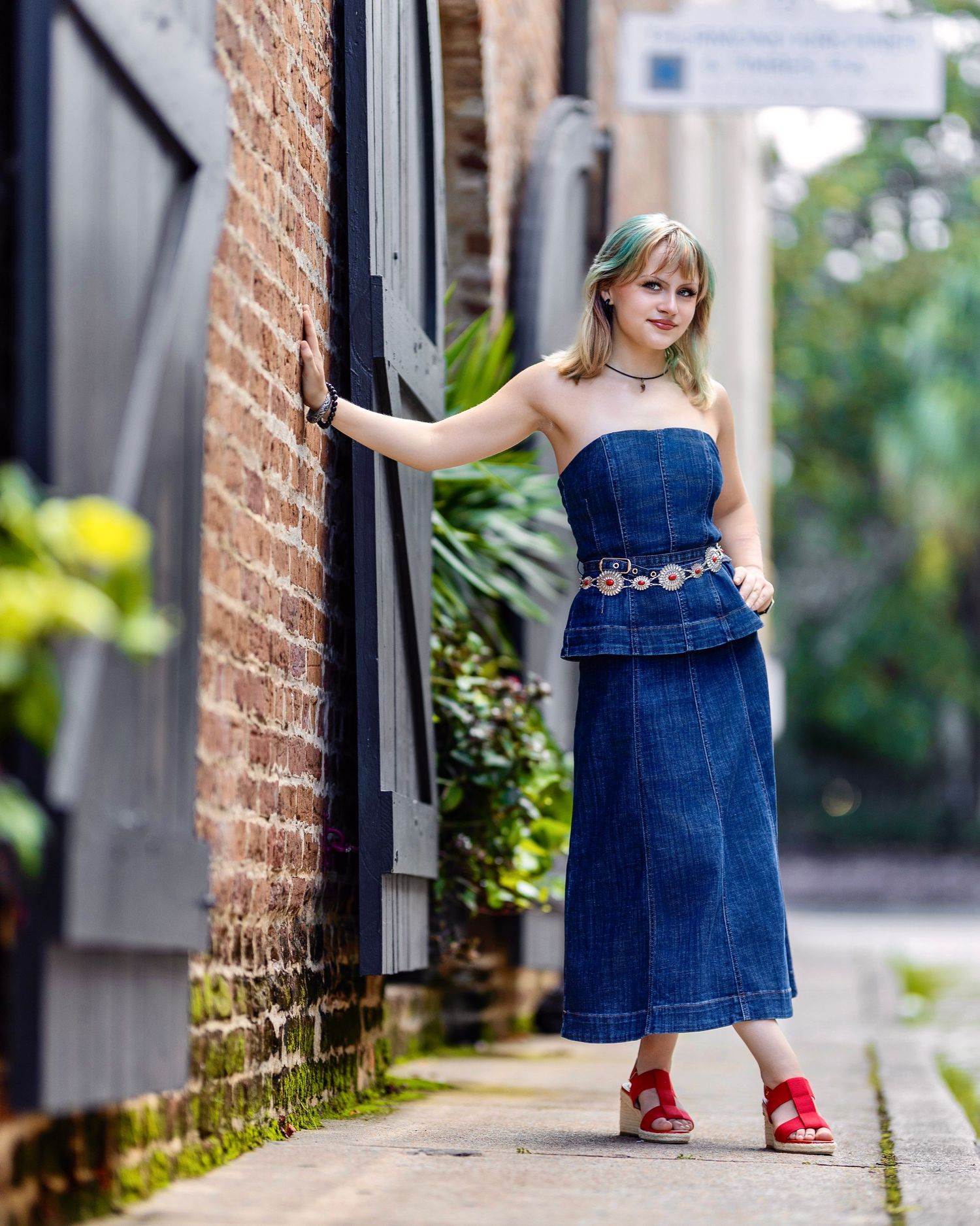 High school senior in a denim outfit posing beside a historic brick building