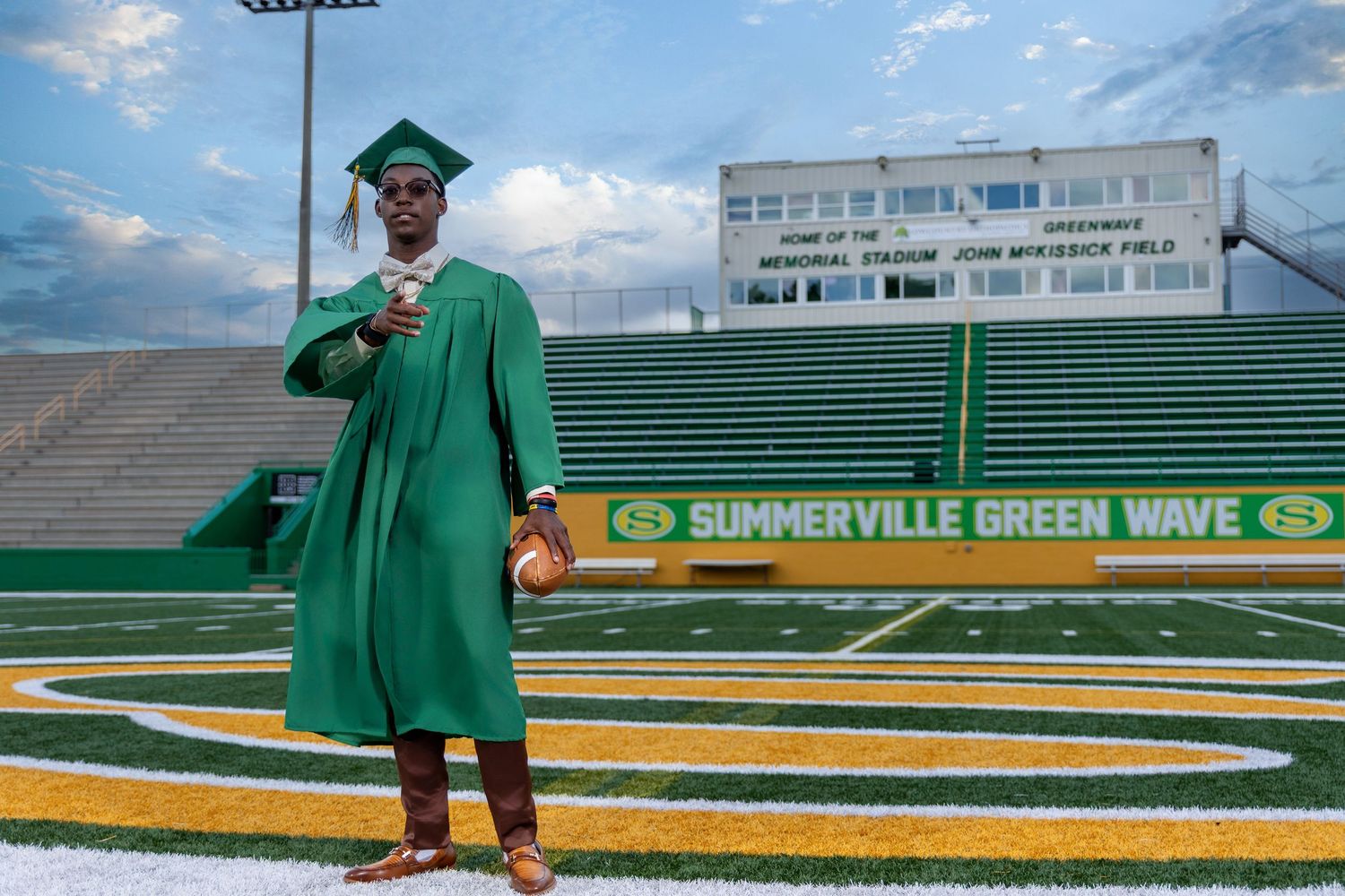 High school senior wearing a green graduation cap and gown on the Summerville Green Wave football field