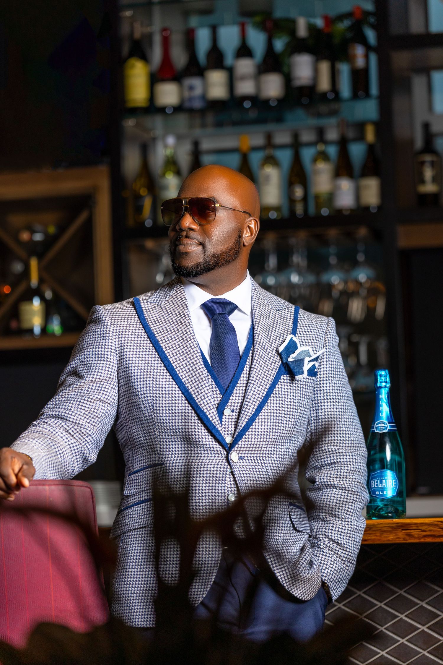 Man wearing a patterned suit and sunglasses posing in a stylish lounge