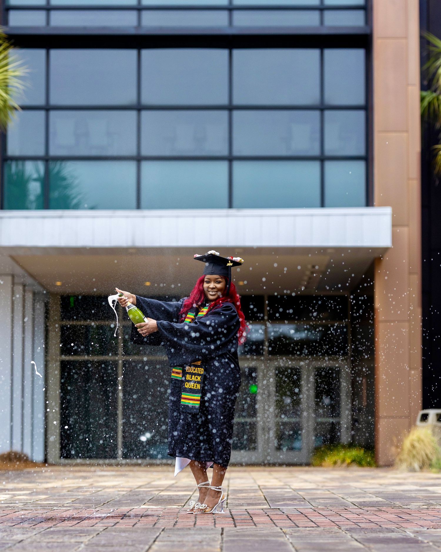 College graduate celebrating with a champagne spray while wearing a cap and gown during a graduation portrait session