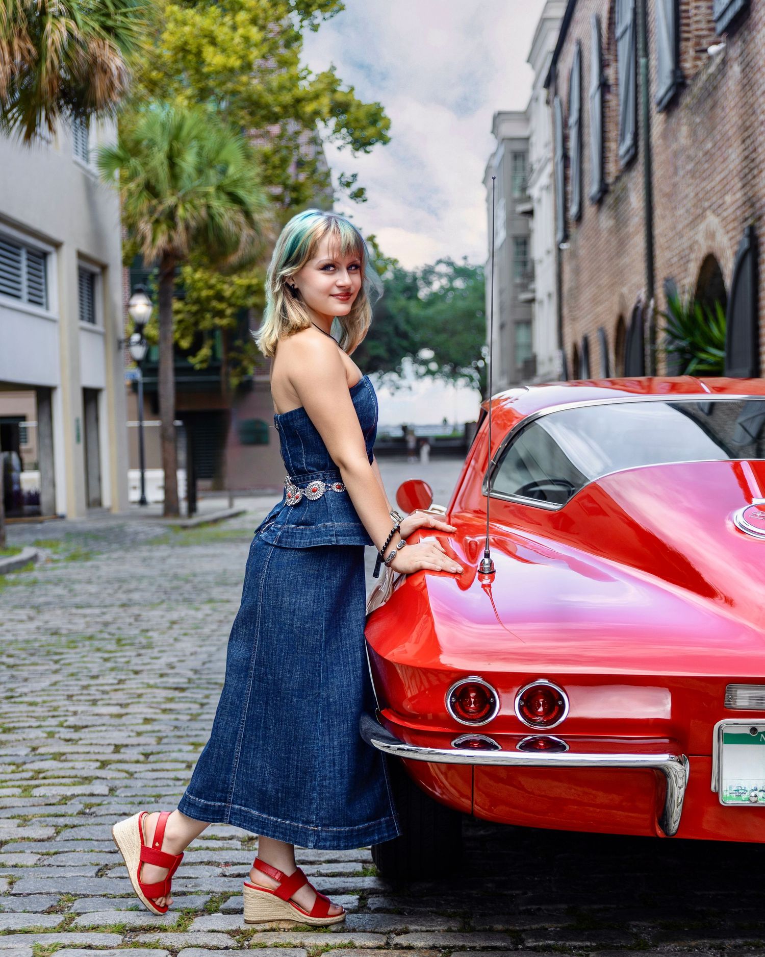High school senior posing beside a classic red Corvette on a cobblestone street