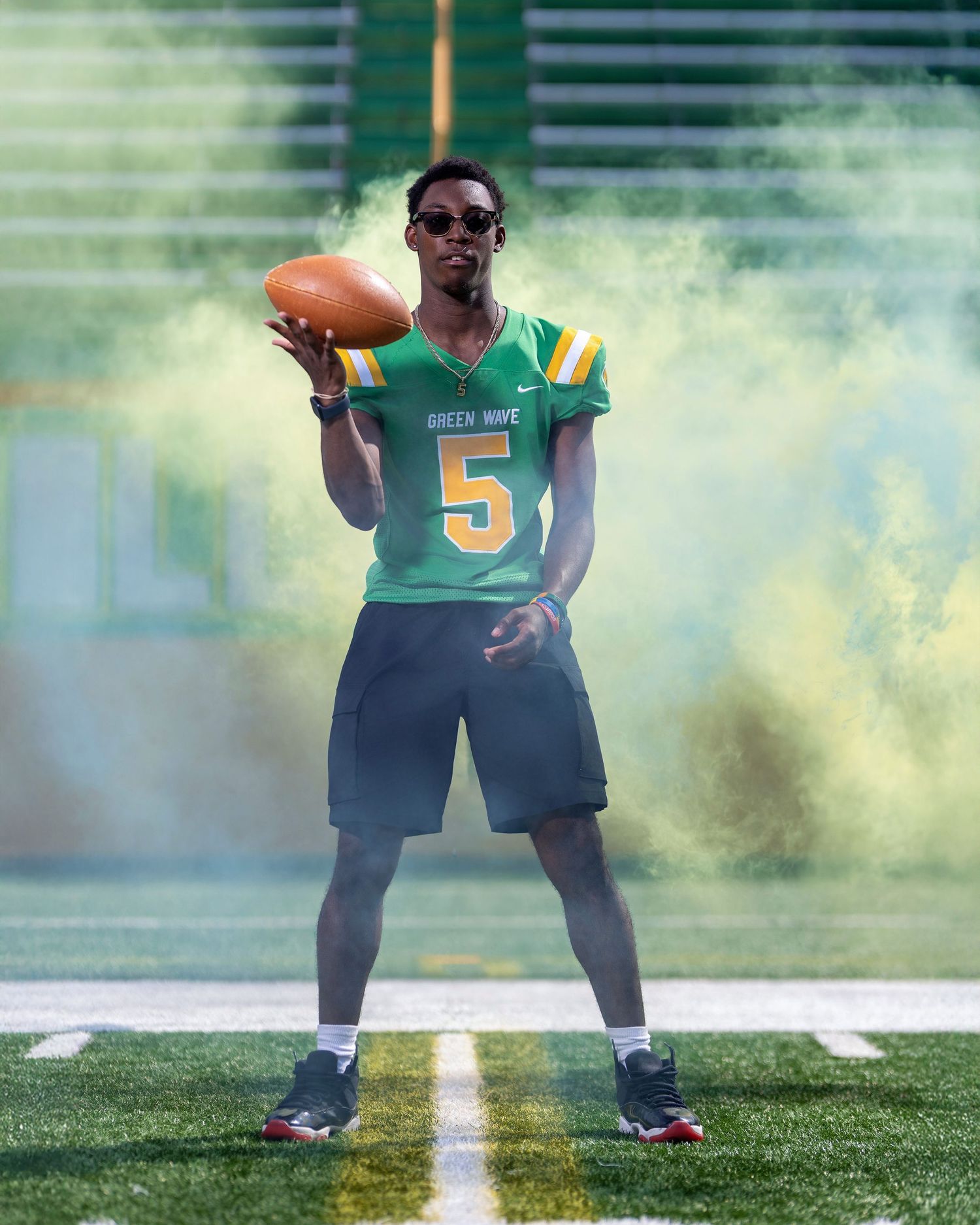 High school football player wearing a Green Wave jersey and holding a football in colored smoke