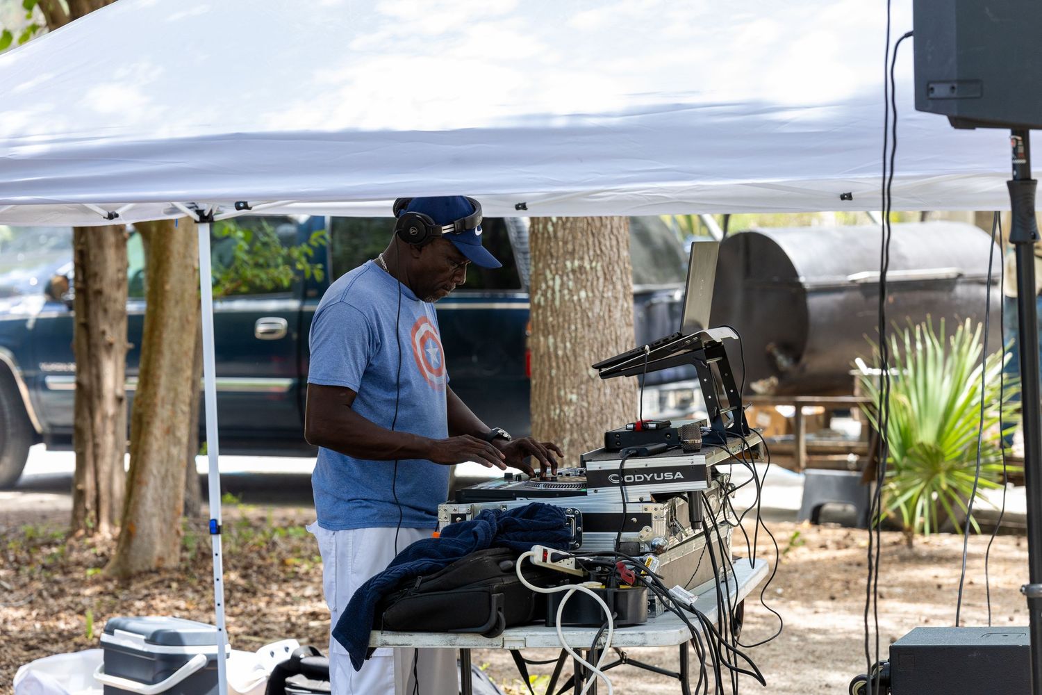 DJ operating mixing equipment under white canopy tent at outdoor family reunion event.