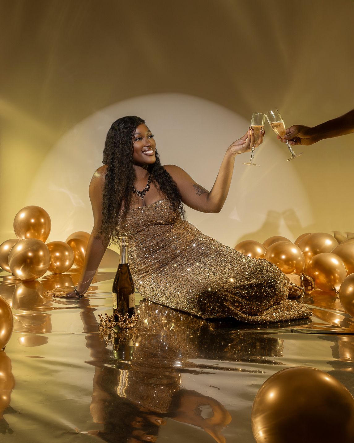 Woman in a sparkling gold gown raising a champagne glass surrounded by gold balloons