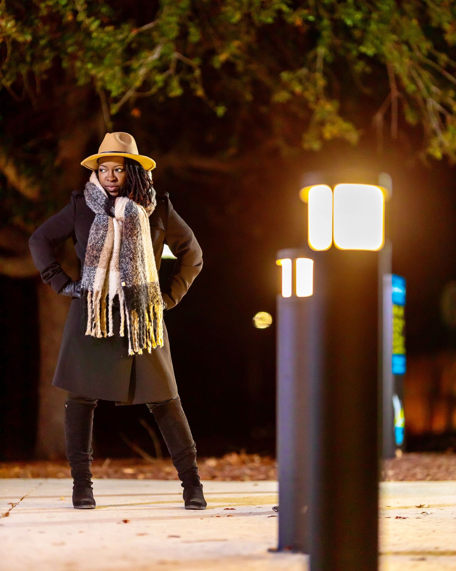 Woman wearing a hat, scarf and coat posing outdoors at night