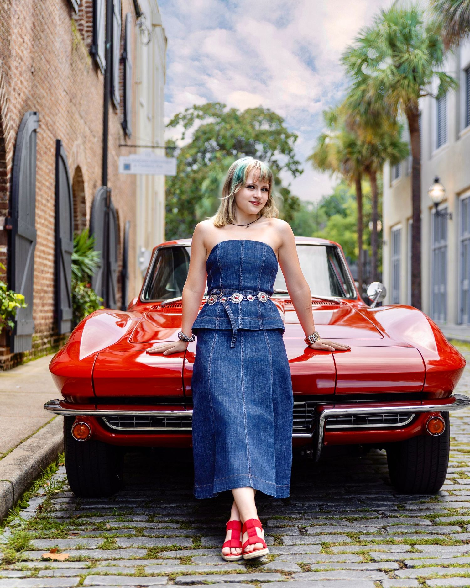 High school senior in a denim outfit posing in front of a classic red Corvette