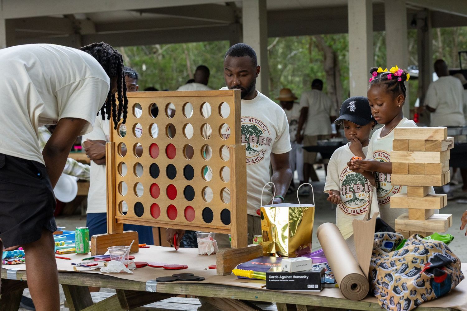 Family reunion attendees play giant Connect Four and Jenga games at outdoor picnic tables.