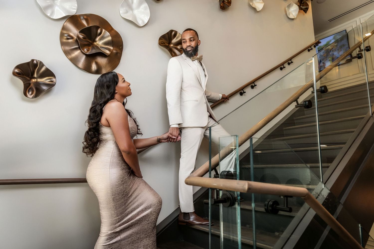 Couple holding hands while walking on a modern staircase in coordinated formal outfits