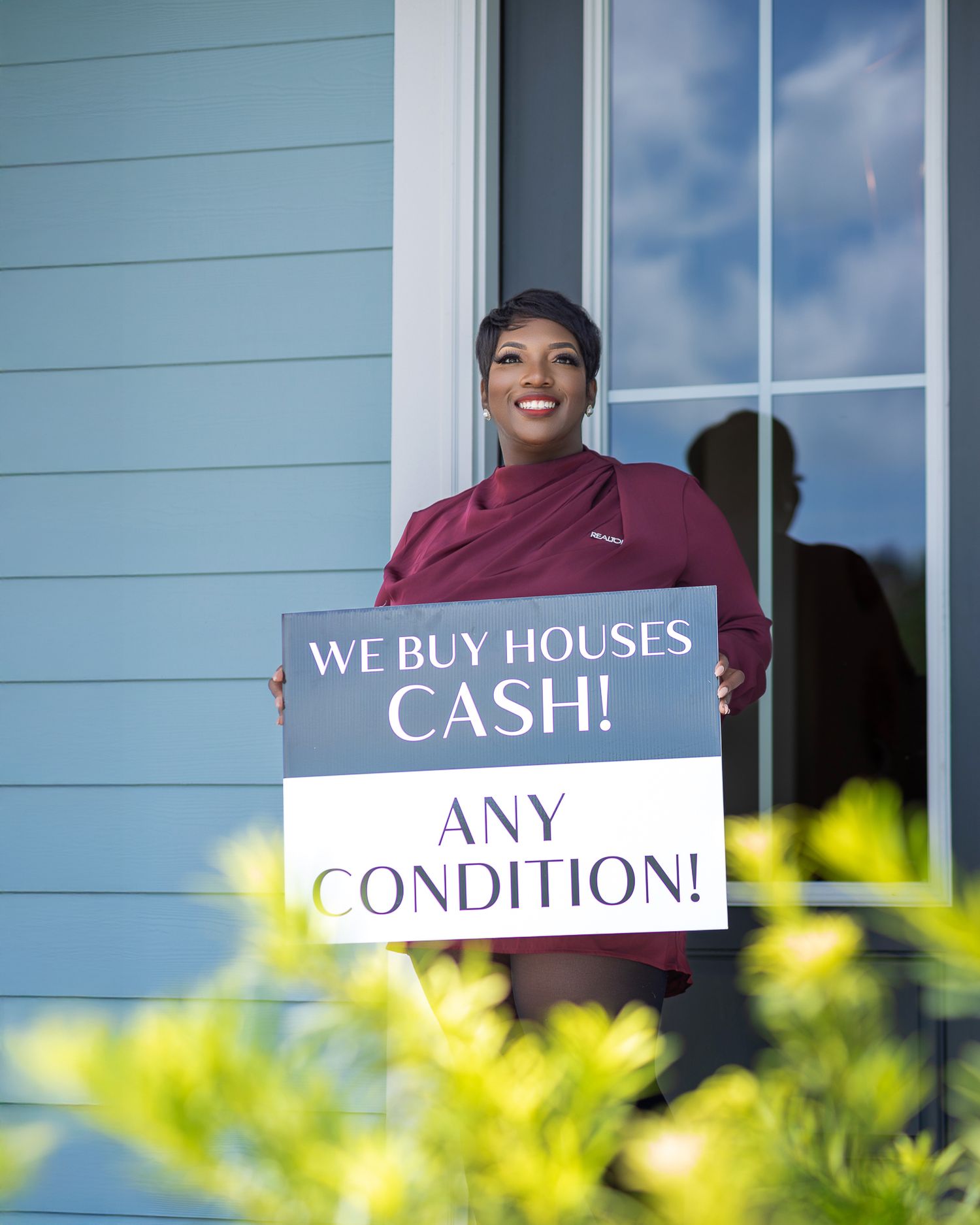 Real estate professional holding a “We Buy Houses Cash” sign outside a home