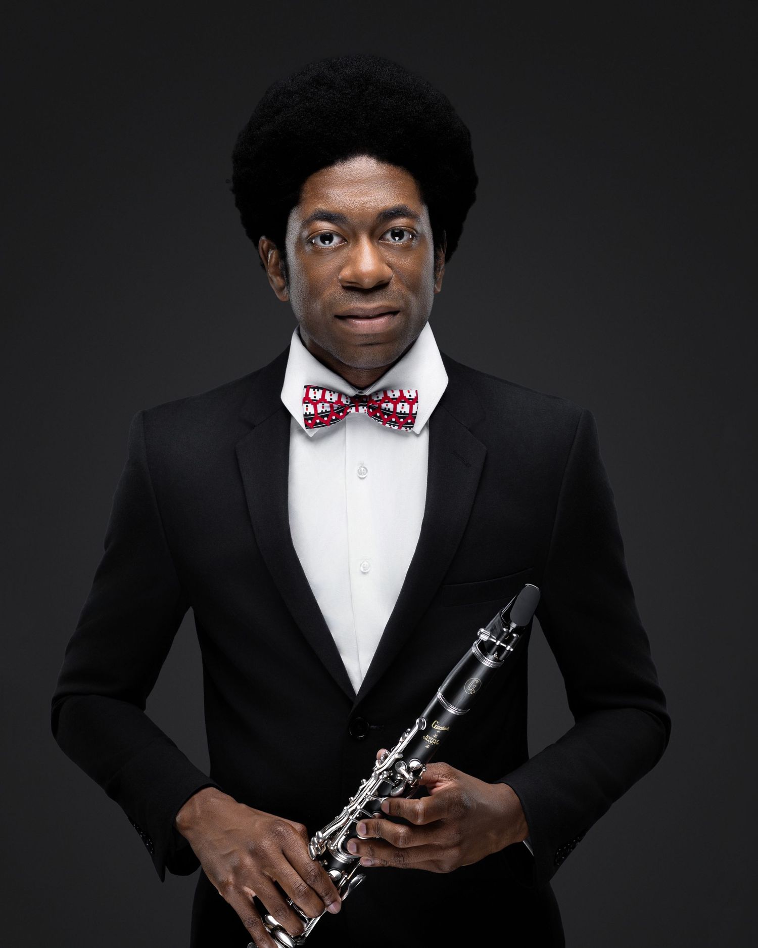 Musician in a black suit and patterned bow tie posing with a clarinet
