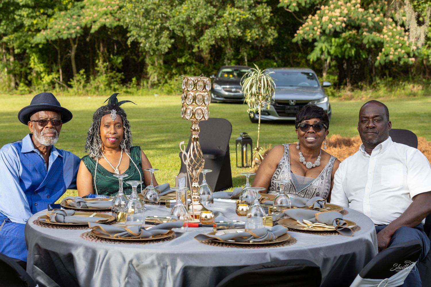 Four guests smile at elegantly decorated outdoor dinner table with gold centerpieces.