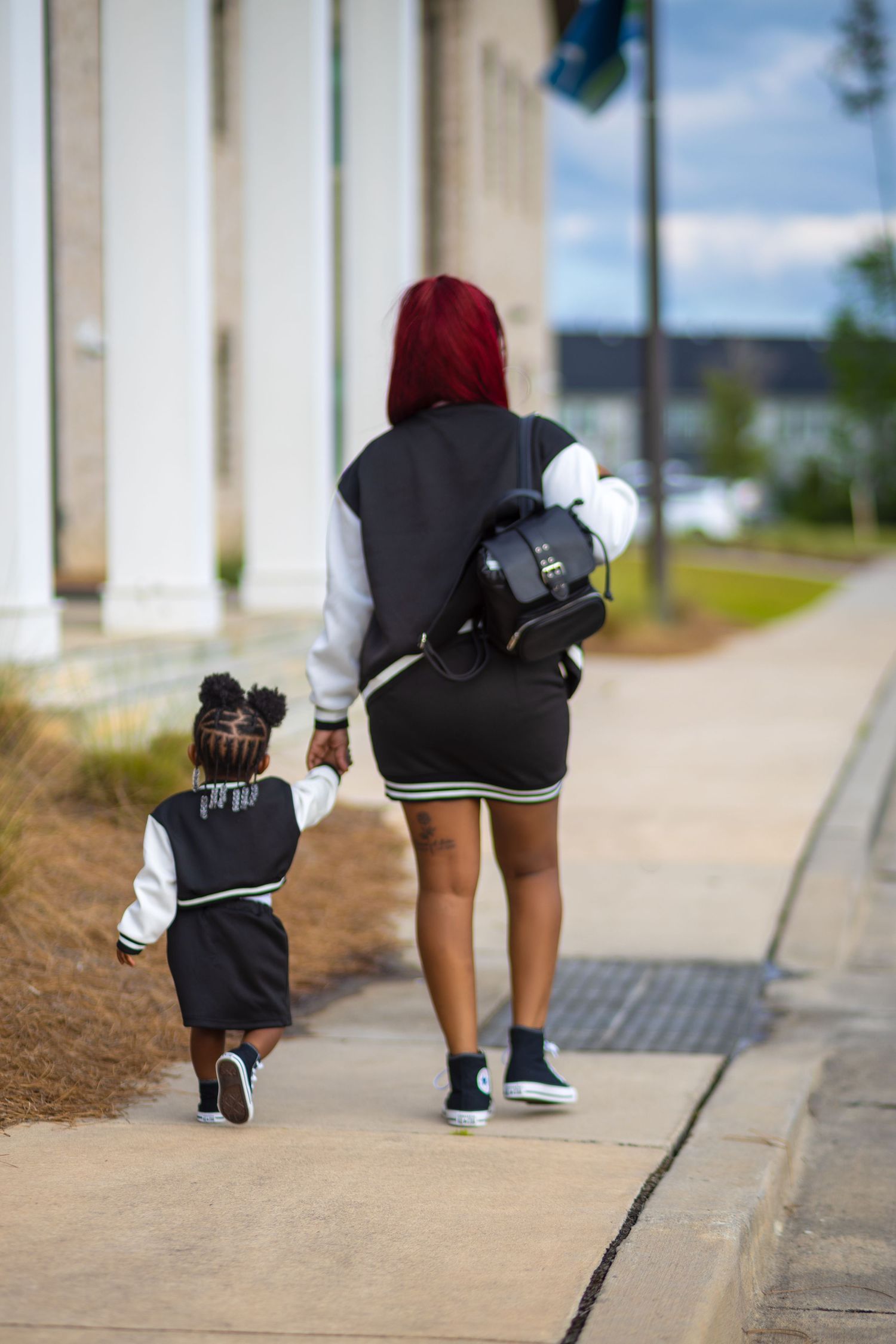 Mother and young daughter walking hand in hand outdoors in matching outfits
