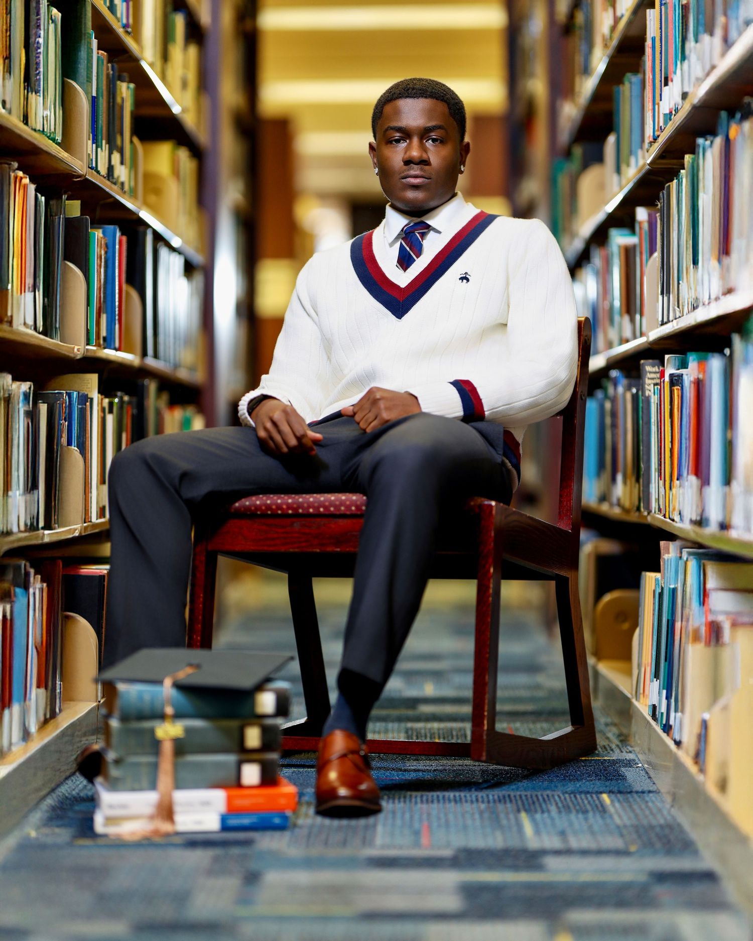 High school senior seated between library bookshelves wearing a white sweater and tie