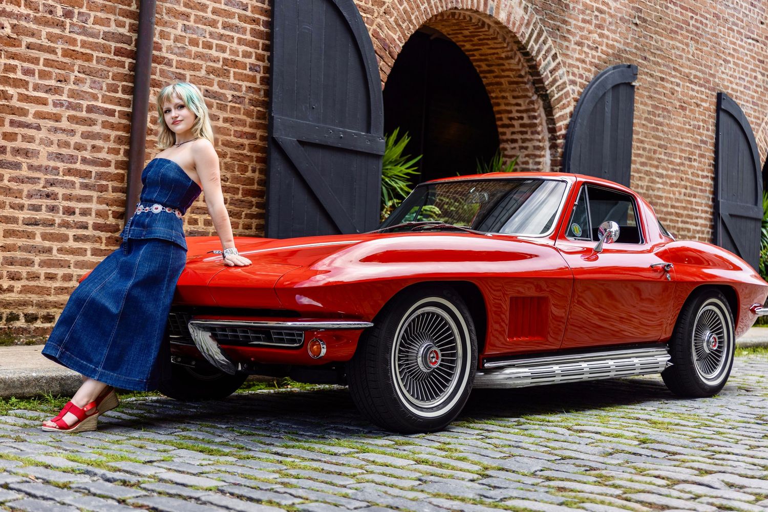 High school senior posing beside a classic red Corvette in front of a historic brick building