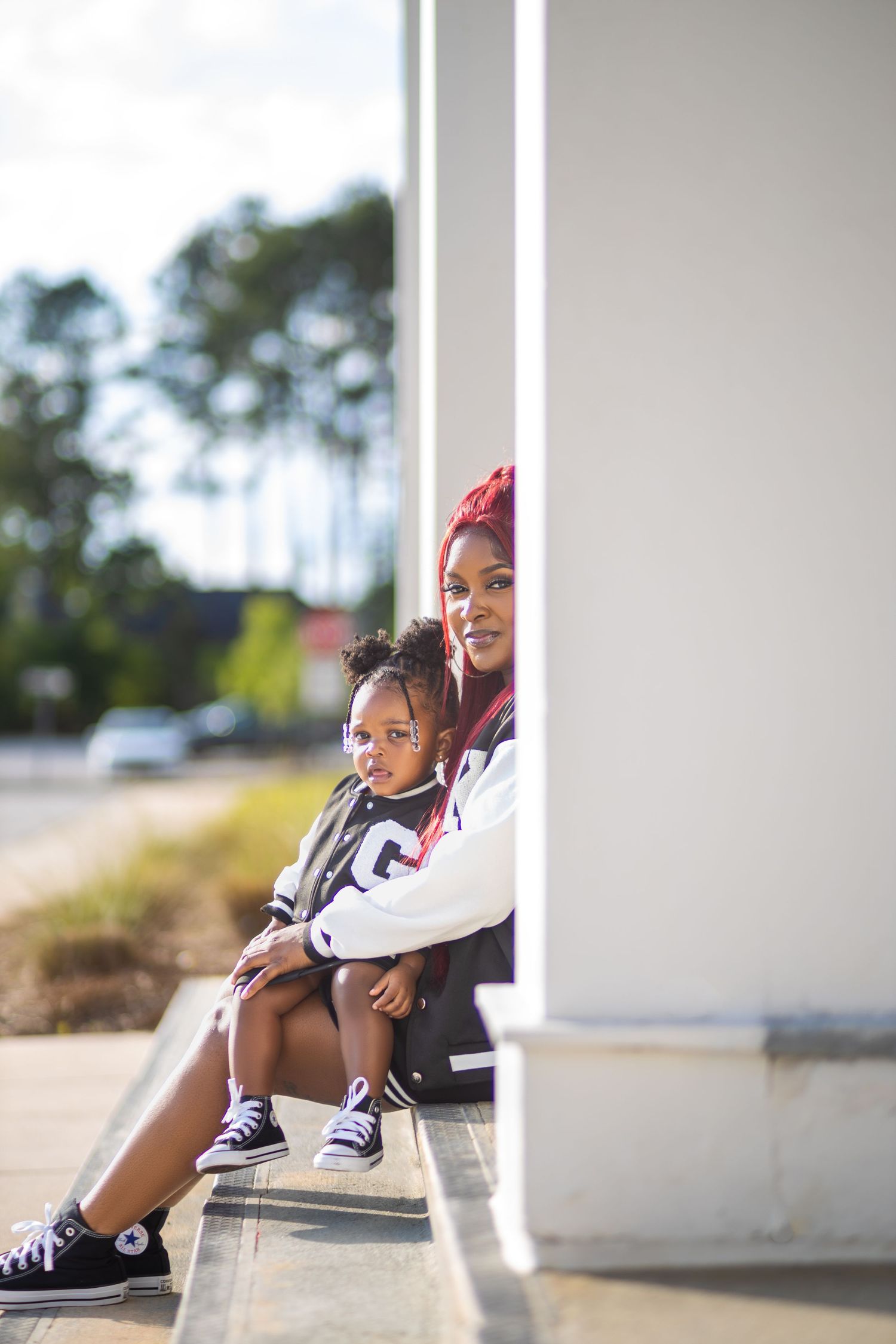 Mother and young daughter sitting together beside a building during an outdoor portrait session