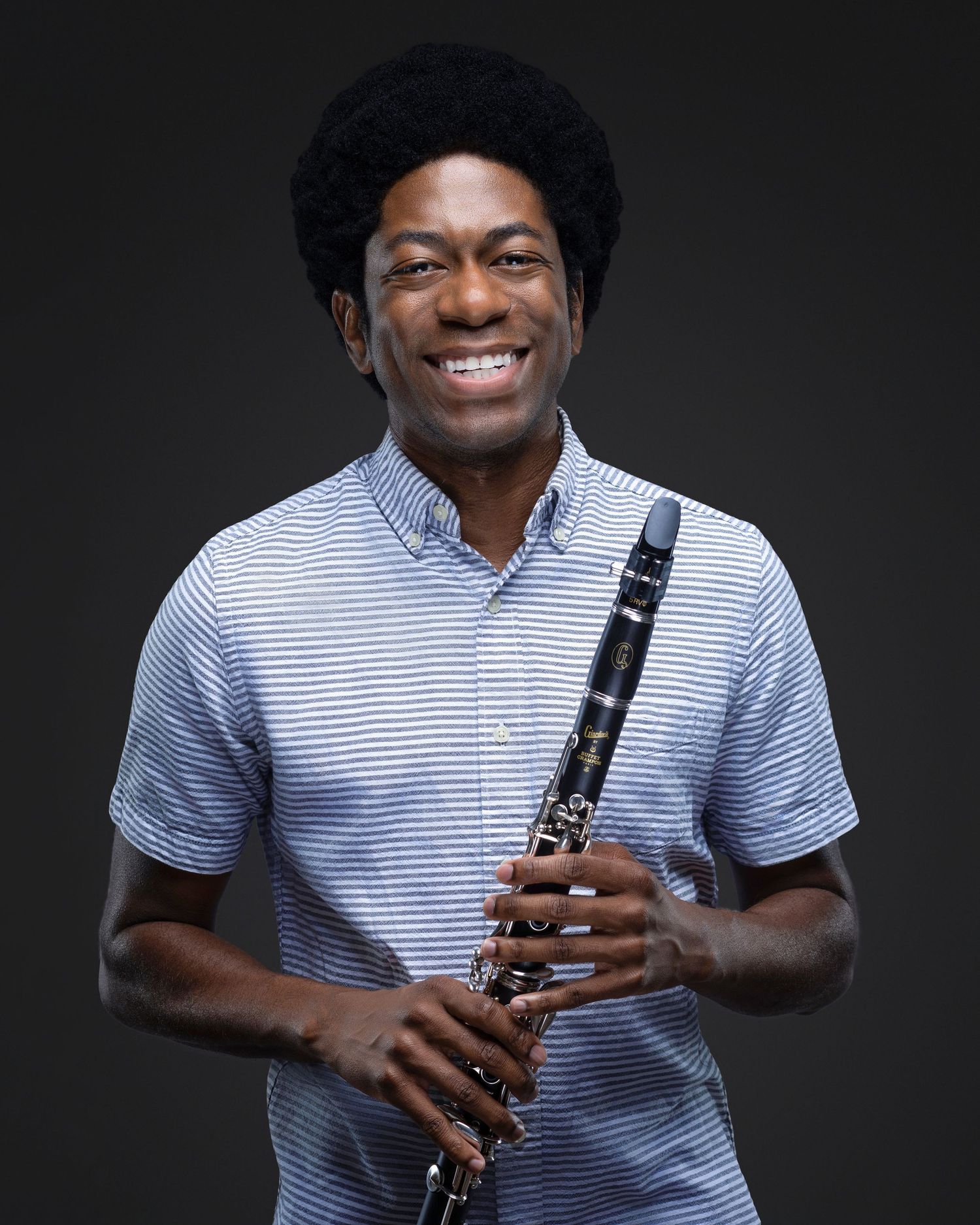 Professional headshot of a man with an instrument posing against a clean studio background.