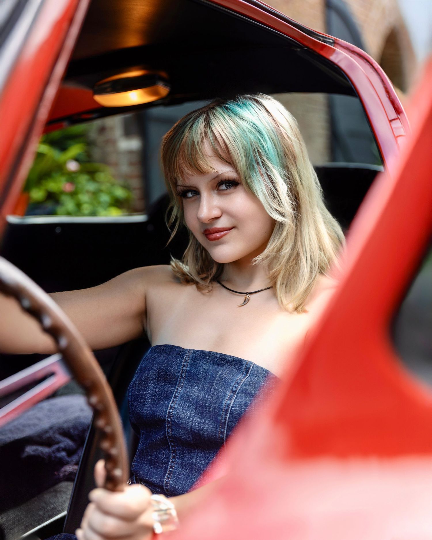 High school senior smiling from the driver's seat of a classic red car