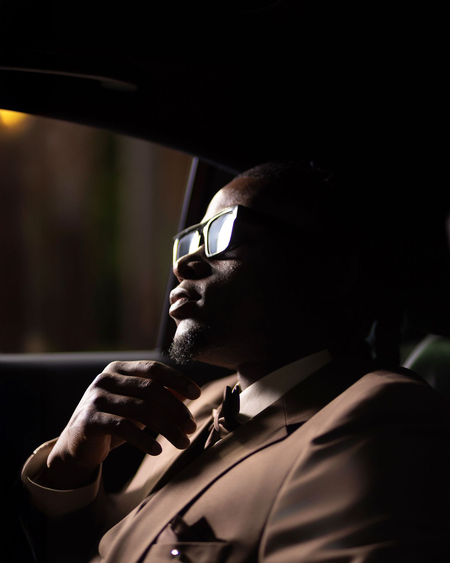 Stylish man in brown suit and glasses sitting in luxury car, contemplative pose at night.