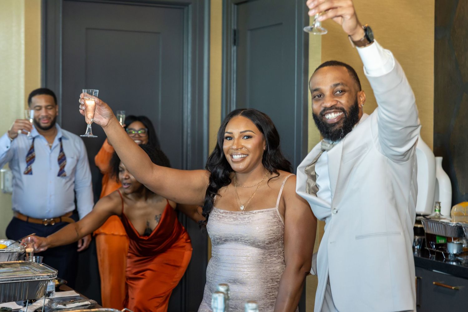 Couple raising champagne glasses in a toast at a festive indoor celebration.