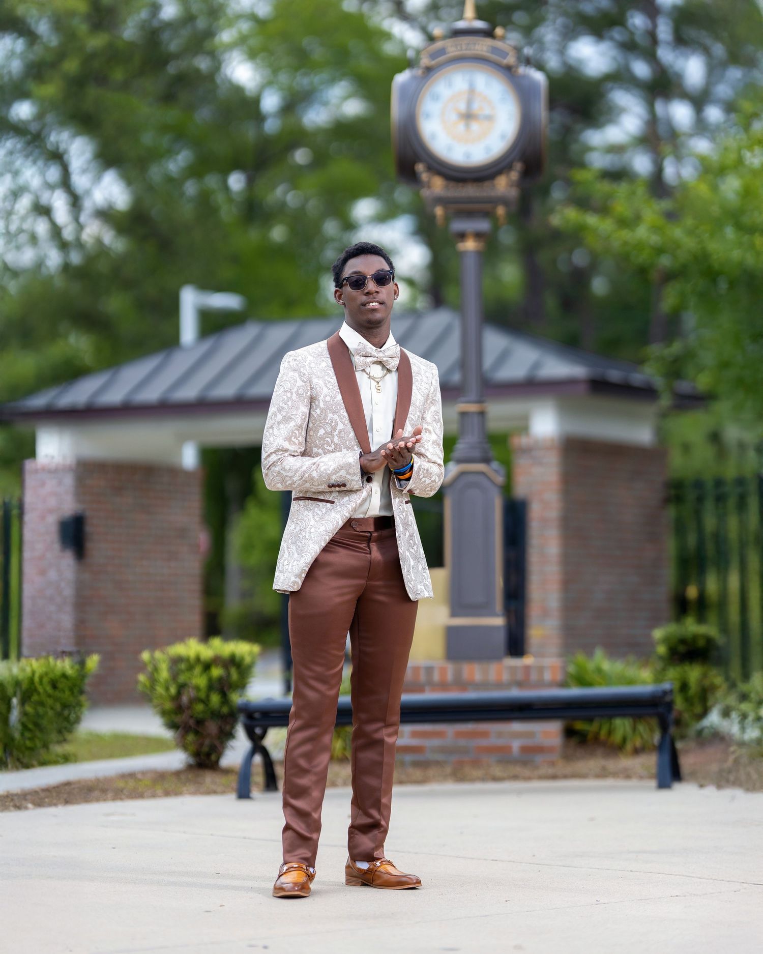 High school senior in a patterned jacket and bow tie posing beside a large outdoor clock