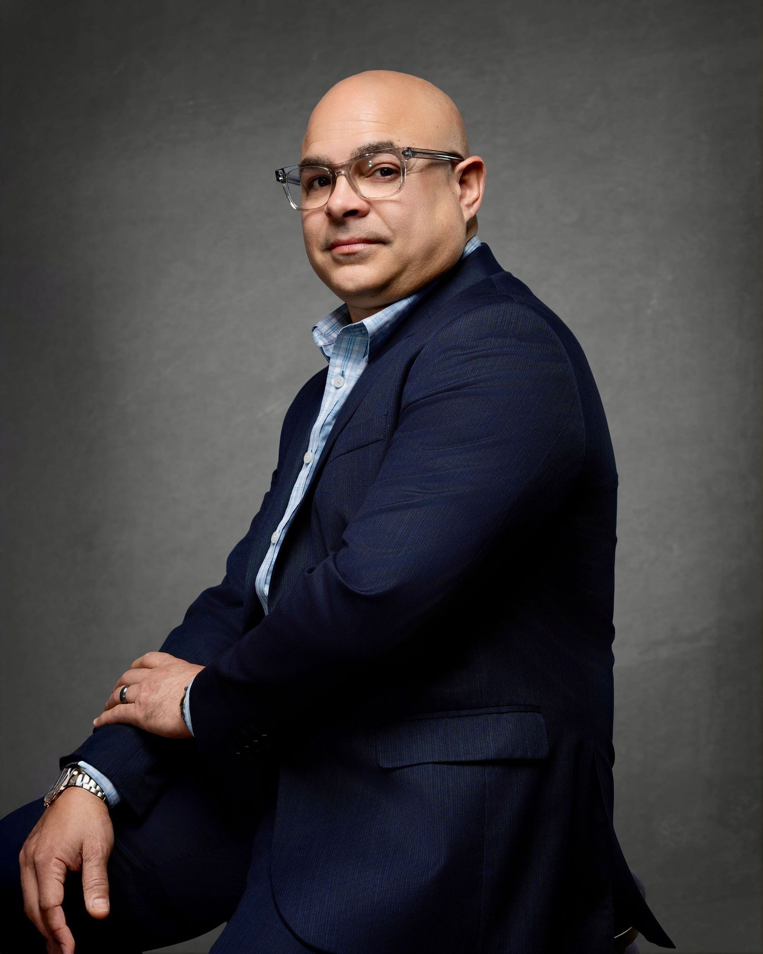 Professional portrait of a man wearing glasses and a navy blazer against a gray background