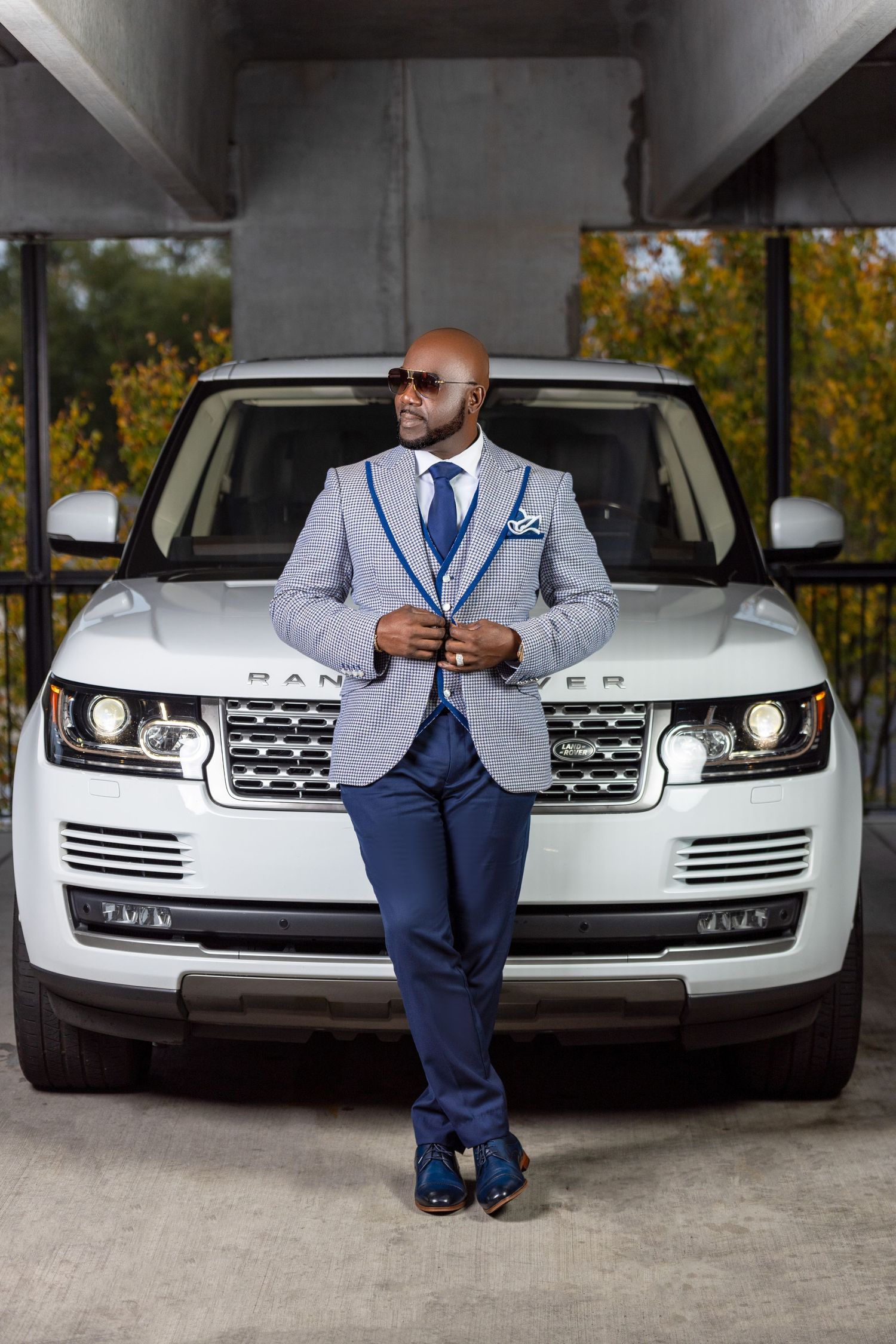 Man in a patterned suit posing in front of a white Range Rover