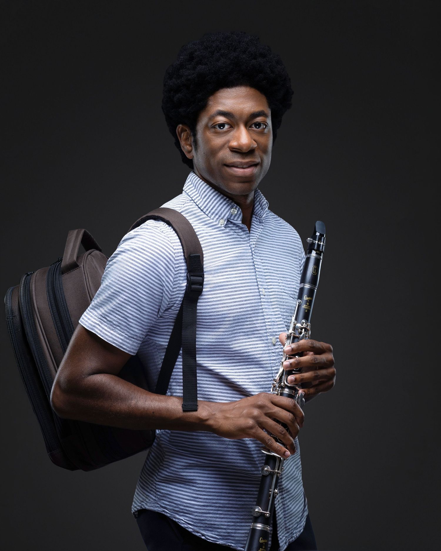 Musician posing with a clarinet and instrument case against a dark studio background