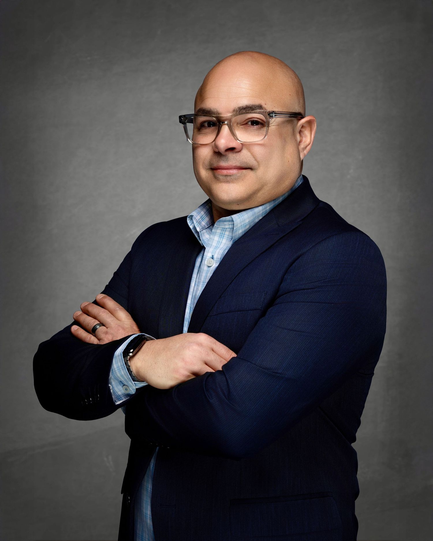Professional portrait of a man wearing glasses and a navy blazer with his arms crossed