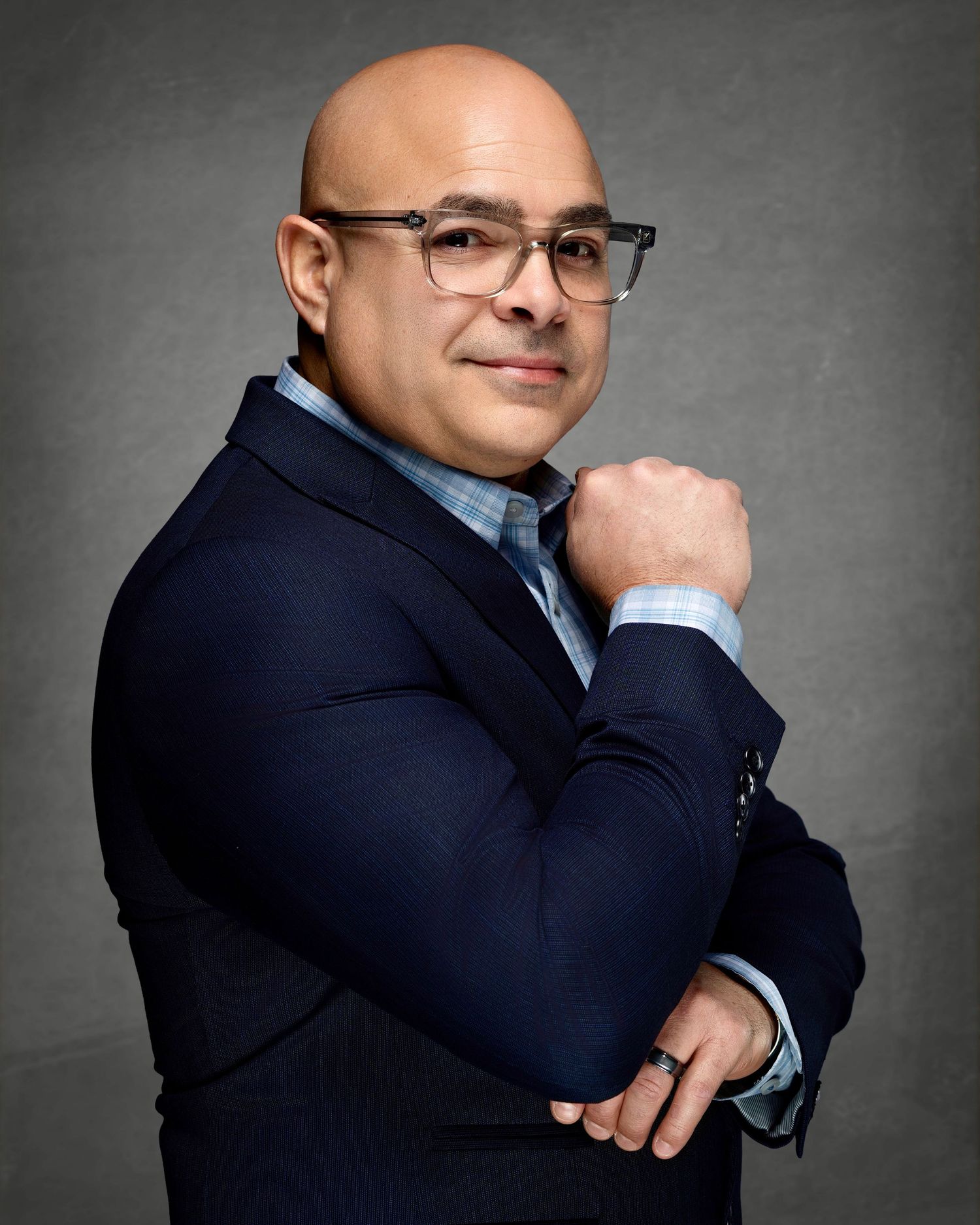 Professional portrait of a man wearing glasses and a navy blazer with his hand near his collar