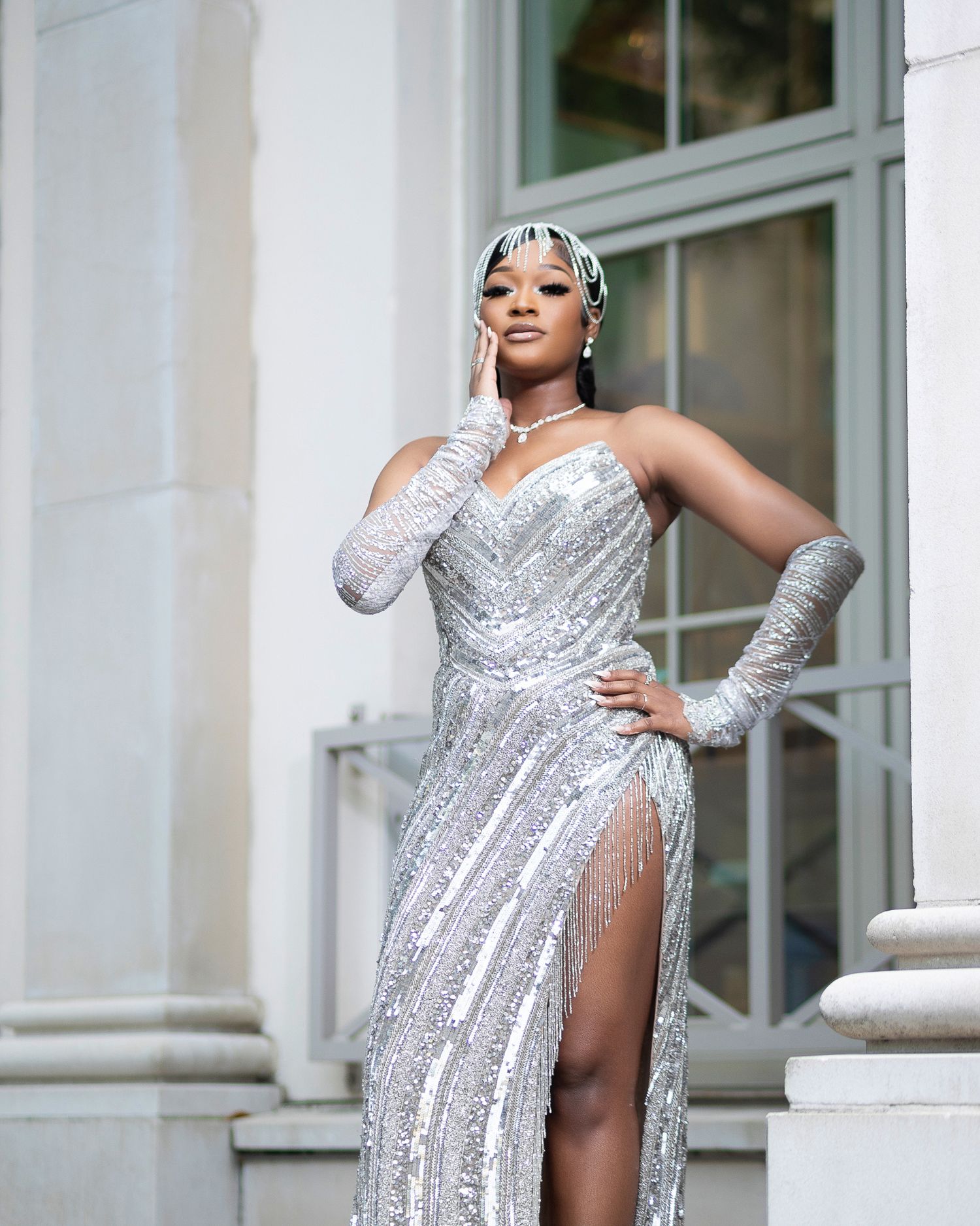Woman in stunning silver sequined gown with matching gloves and headpiece posing outdoors.