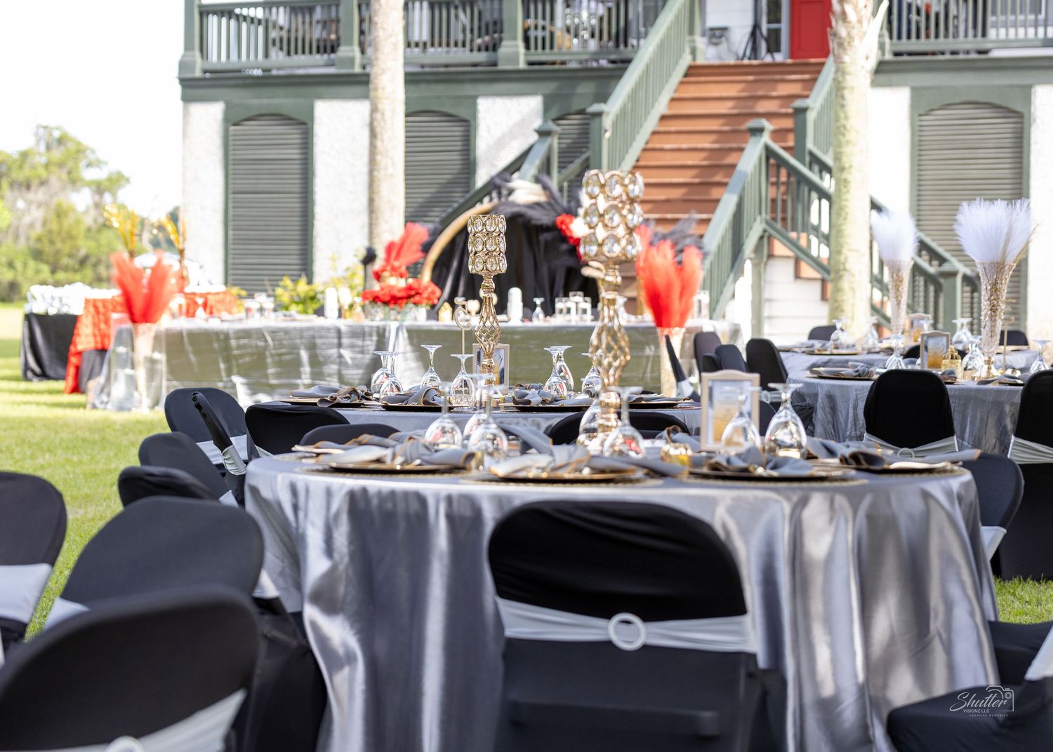 Sophisticated outdoor event setup with silver and black table settings on green lawn.