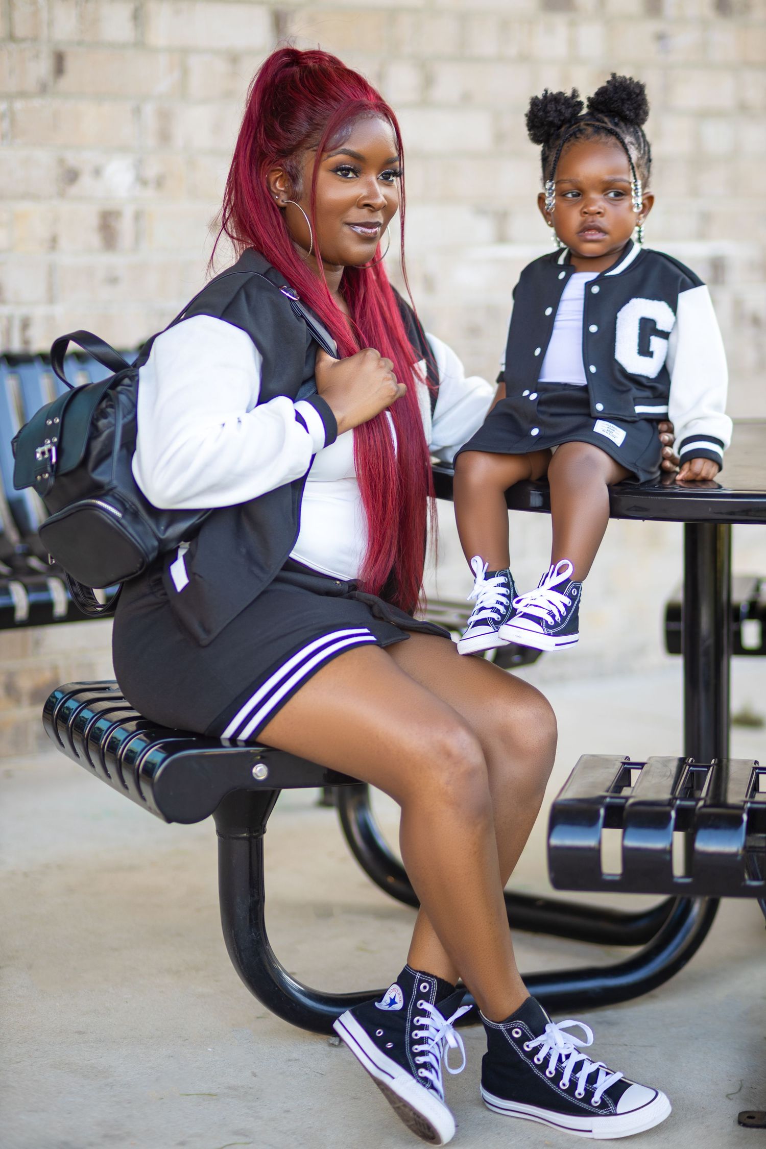 Mother and young daughter sitting together outdoors in matching varsity-style outfits