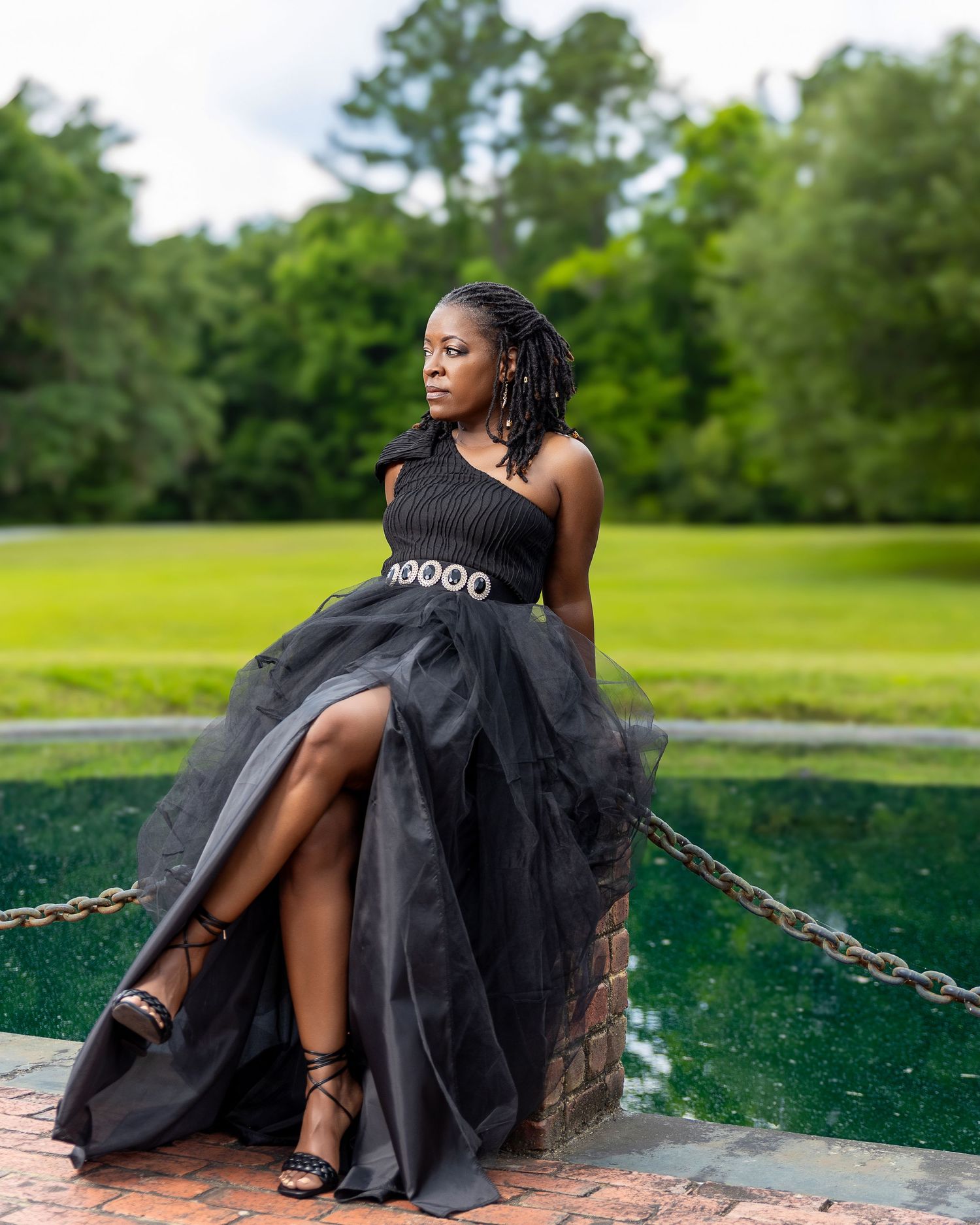 Woman in a black gown sitting beside a landscaped pond during an elegant portrait session