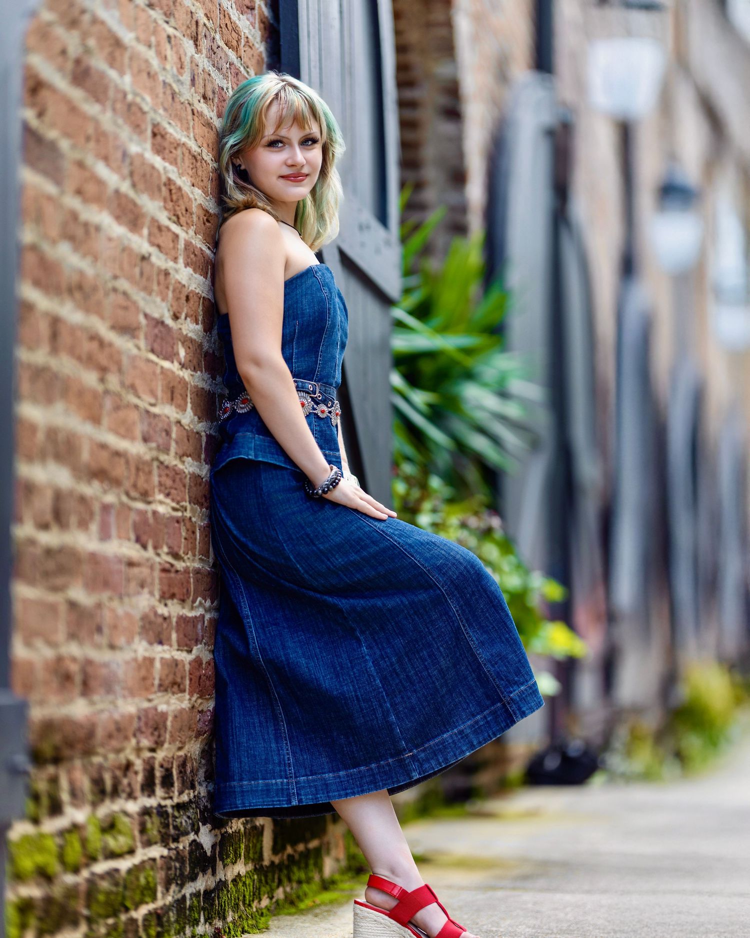 High school senior in a denim outfit leaning against a historic brick wall