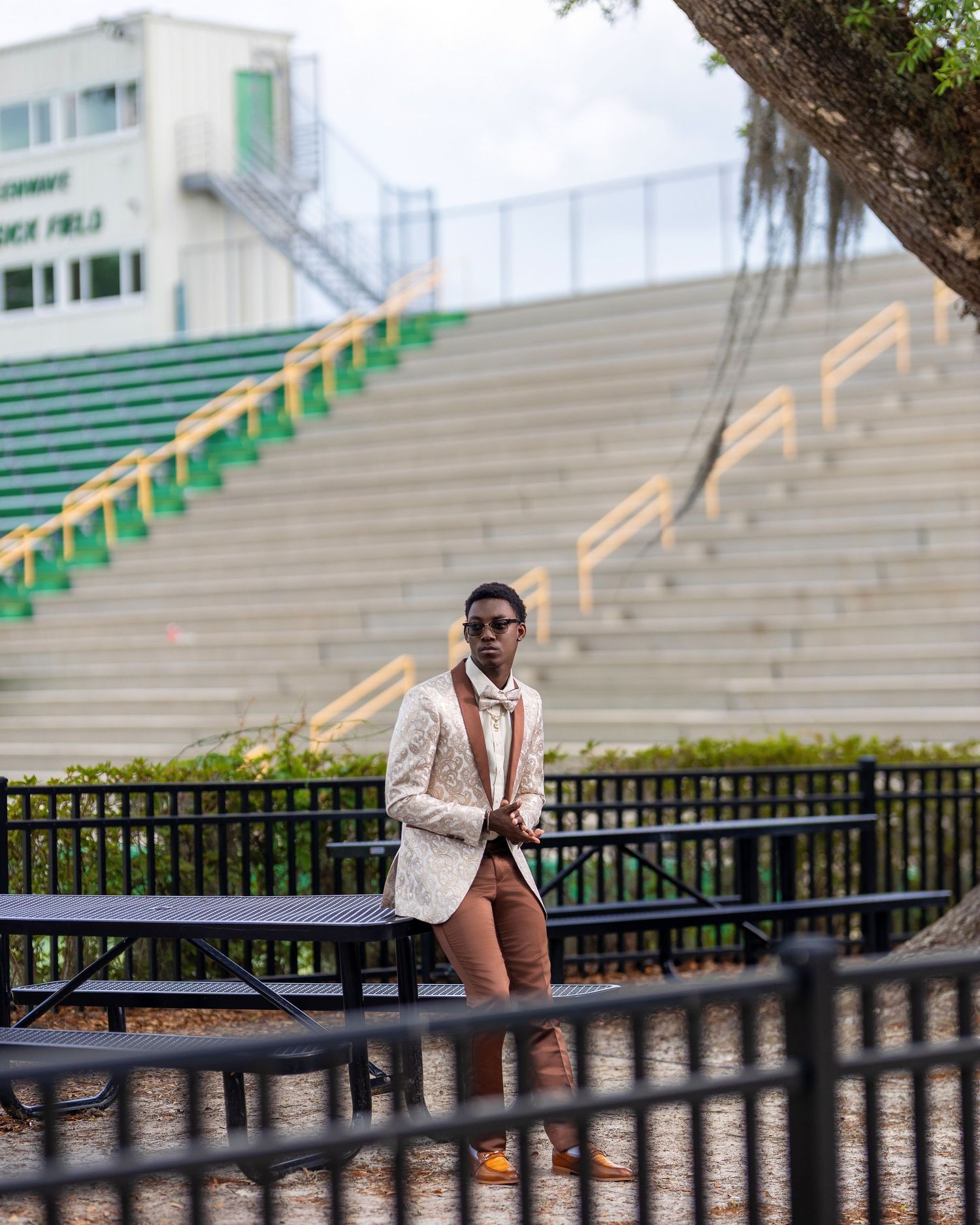High school senior in a patterned jacket and bow tie posing in front of football stadium bleachers