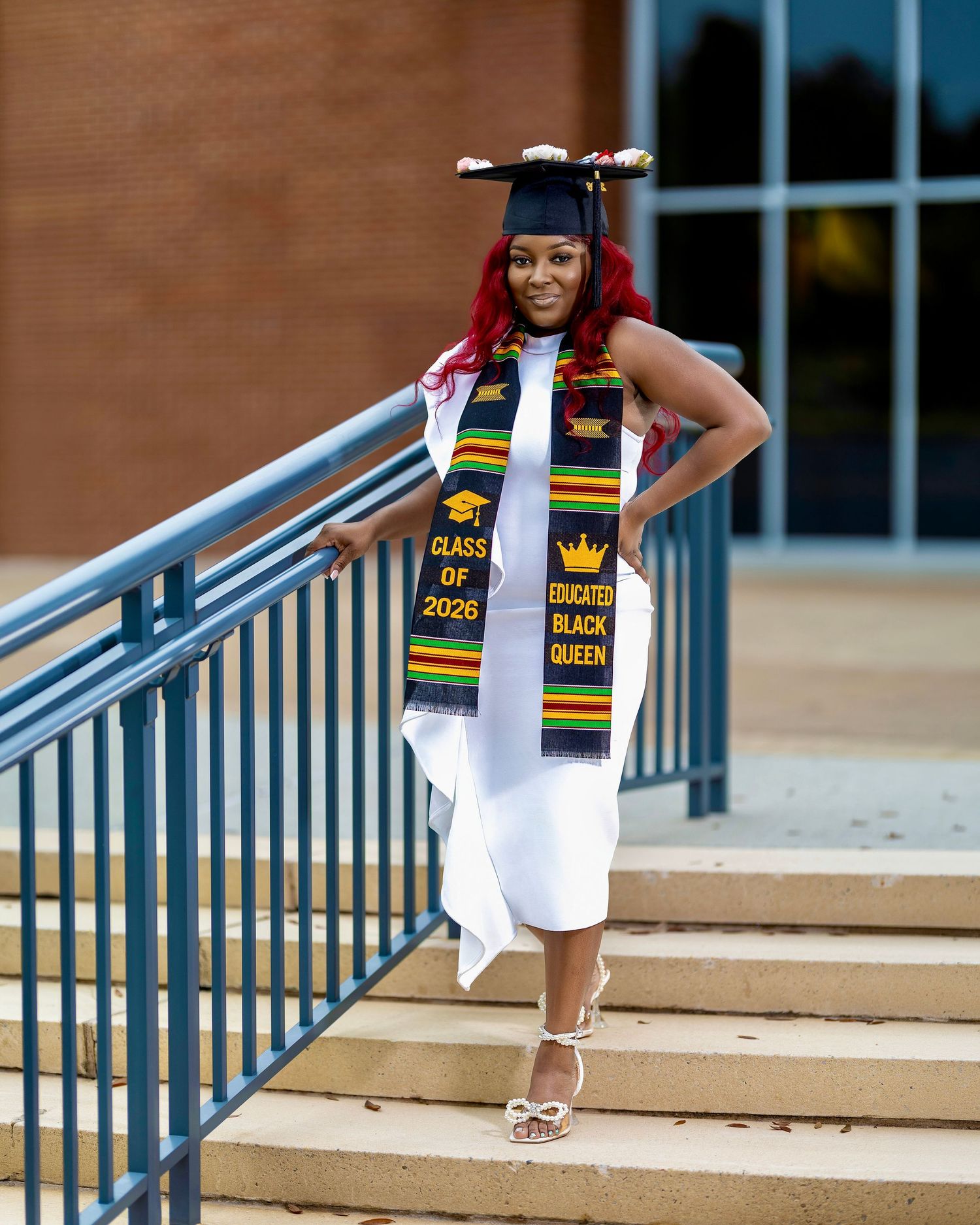 College graduate in a white dress and decorated cap posing on outdoor steps