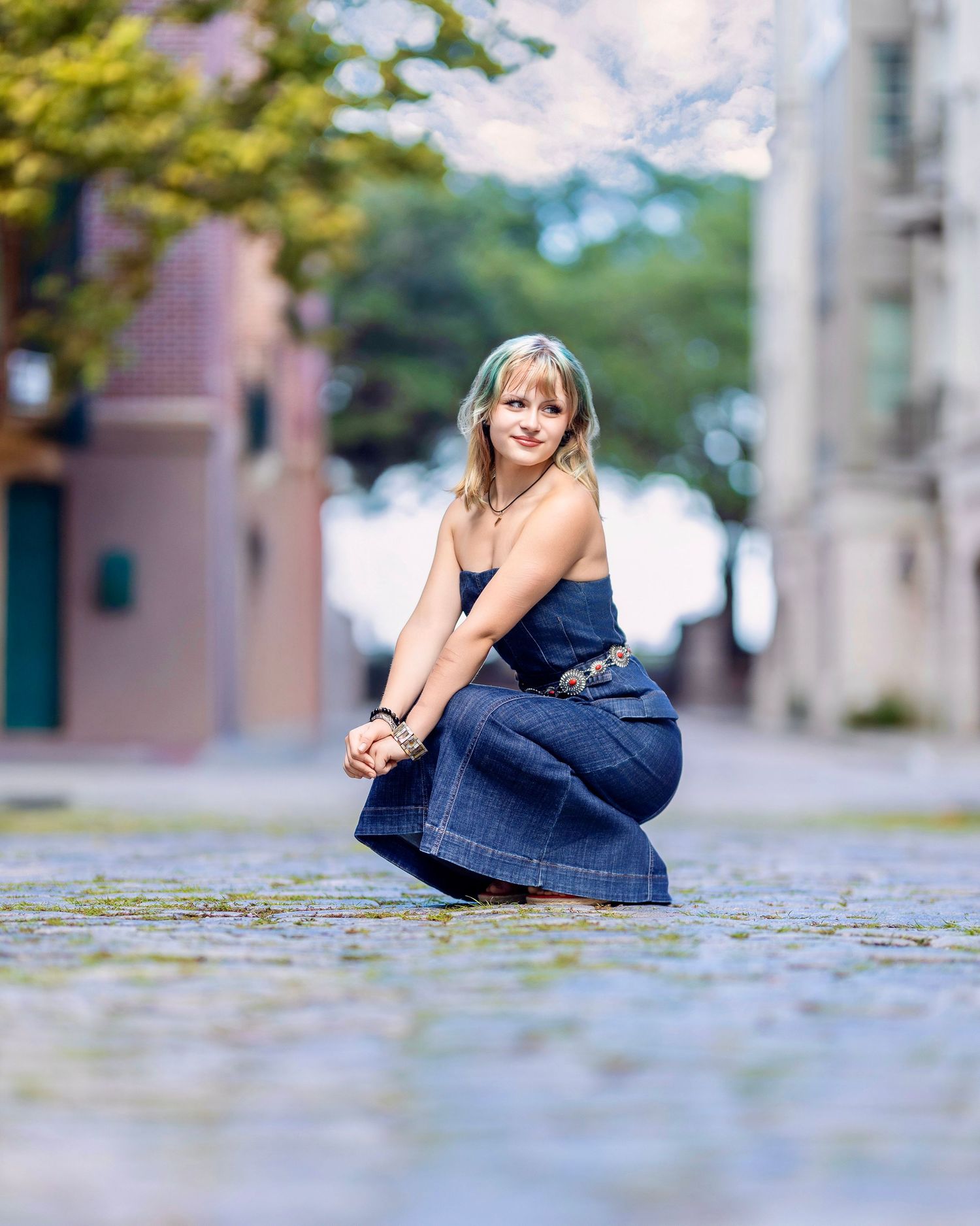 High school senior posing in a denim outfit kneeling down on a cobblestone Charleston street