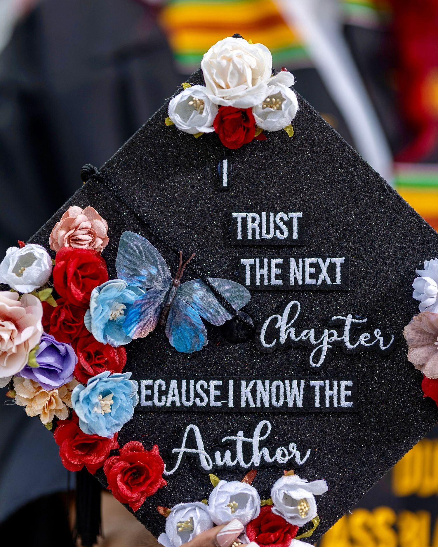 Decorated black graduation cap covered with flowers and the words “Trust the Next Chapter”