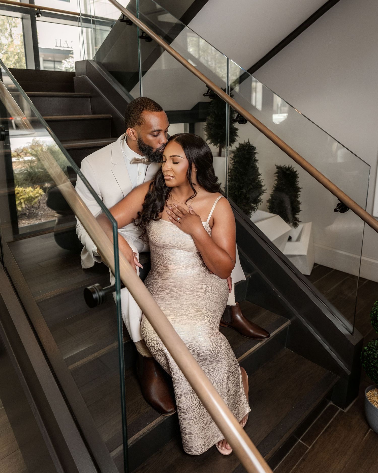 Couple in elegant white and champagne-colored outfits embracing on a modern staircase