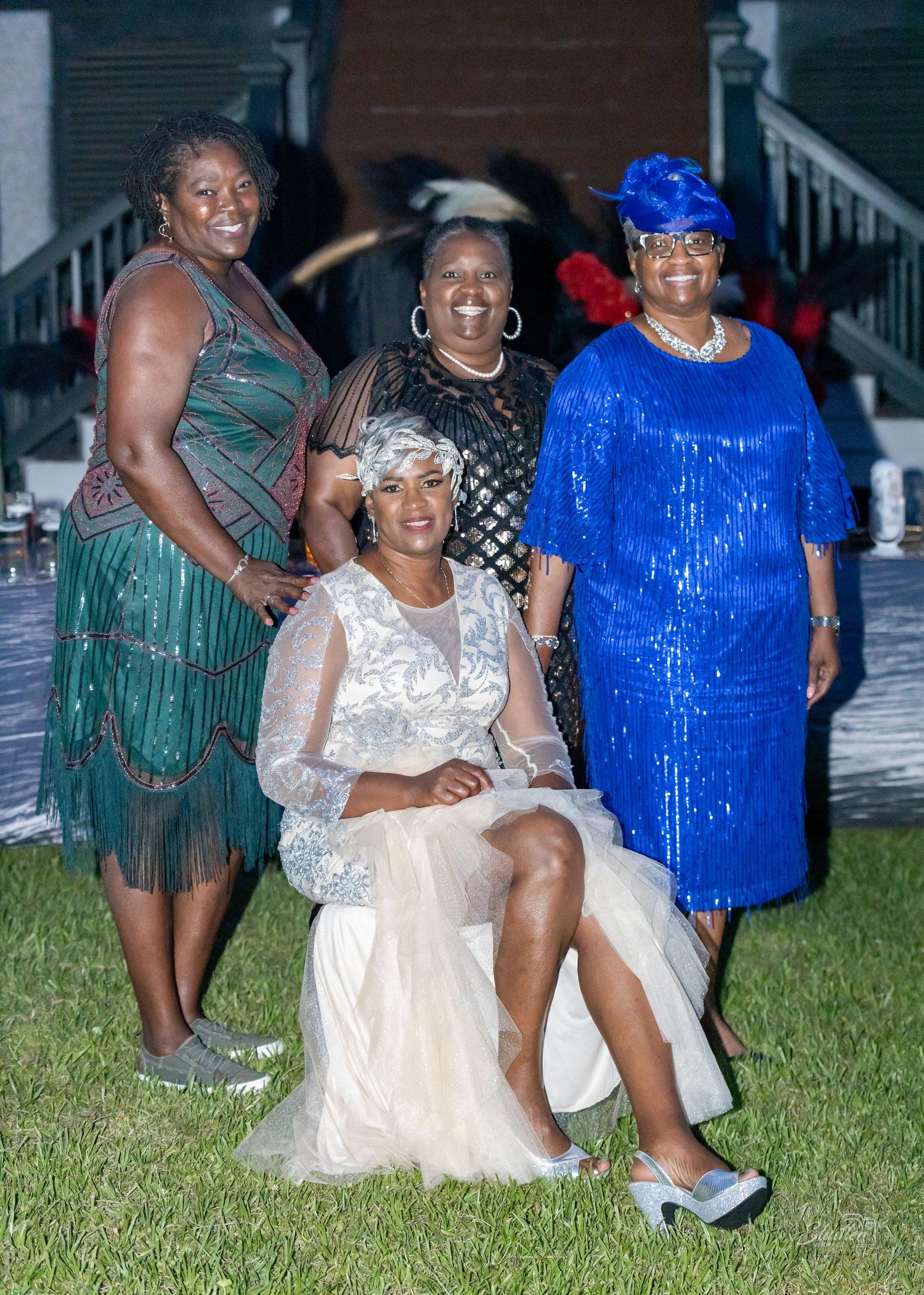 Four women in elegant vintage-inspired outfits pose together outdoors at a formal evening event.