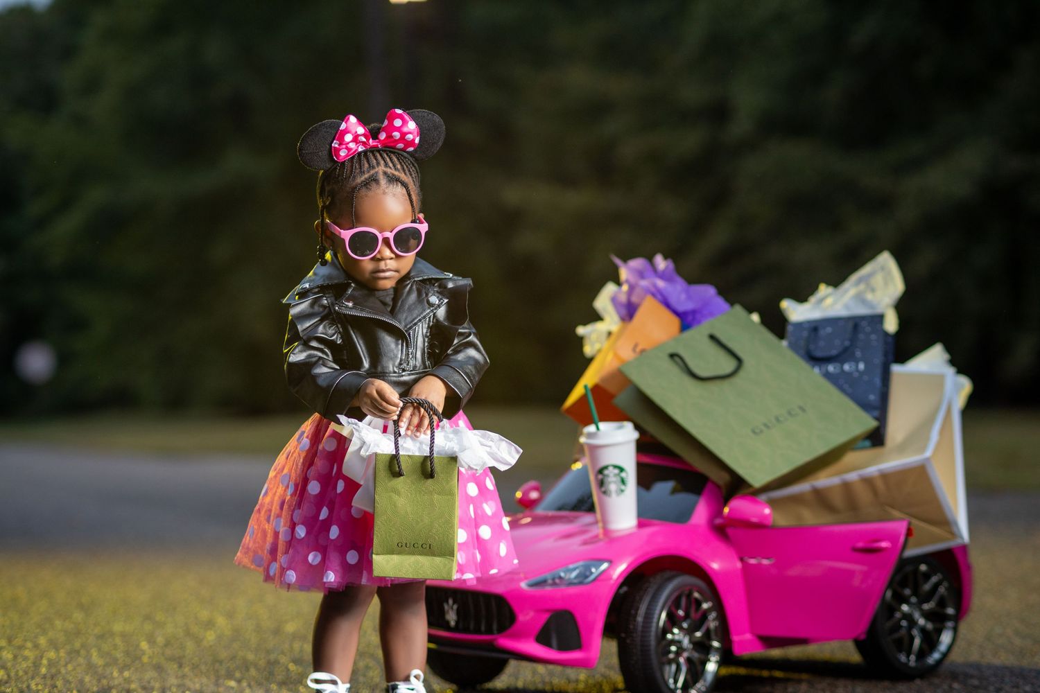 Adorable girl in Minnie Mouse outfit holds shopping bags beside pink toy car.