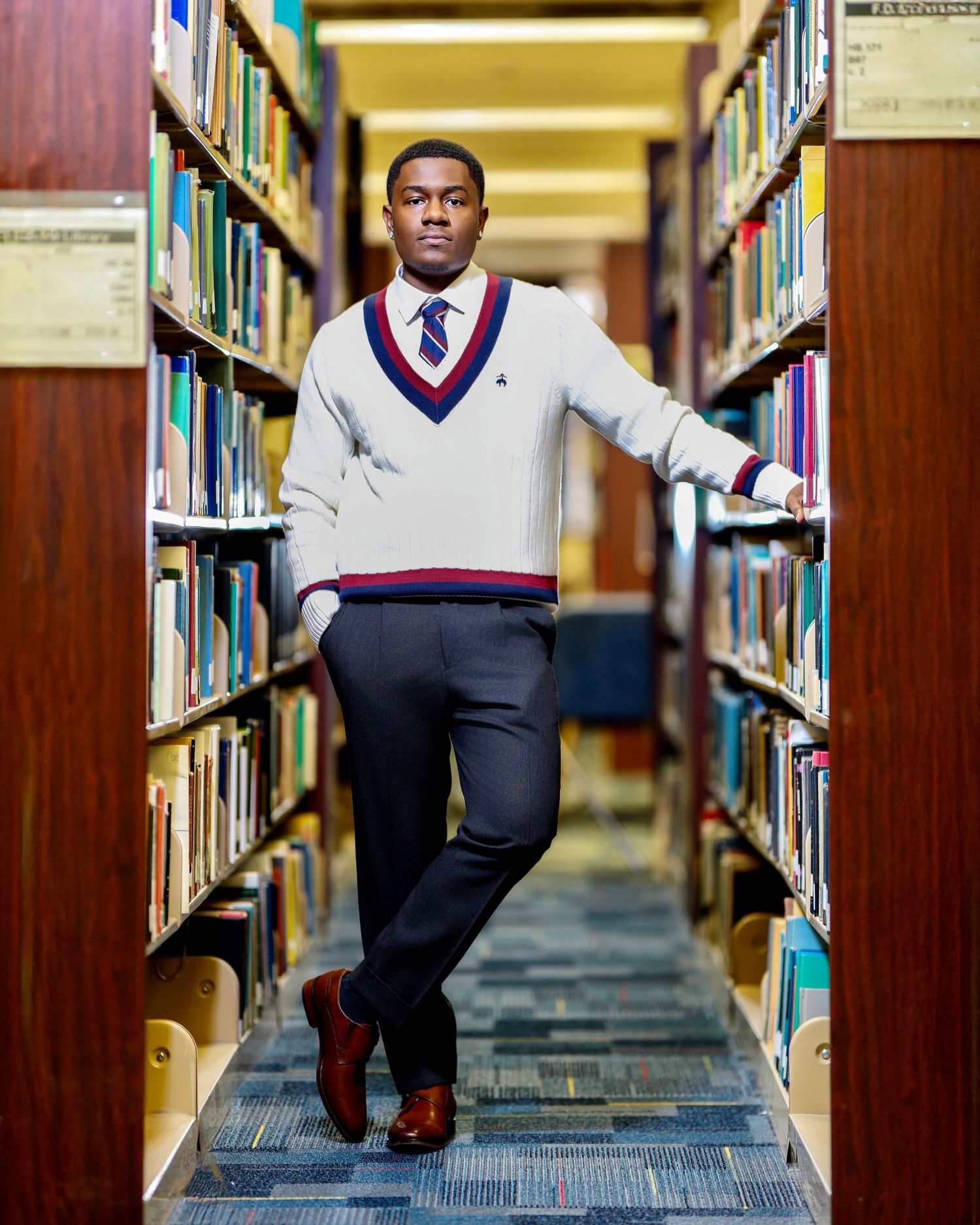 High school senior standing between library bookshelves in a white sweater and tie