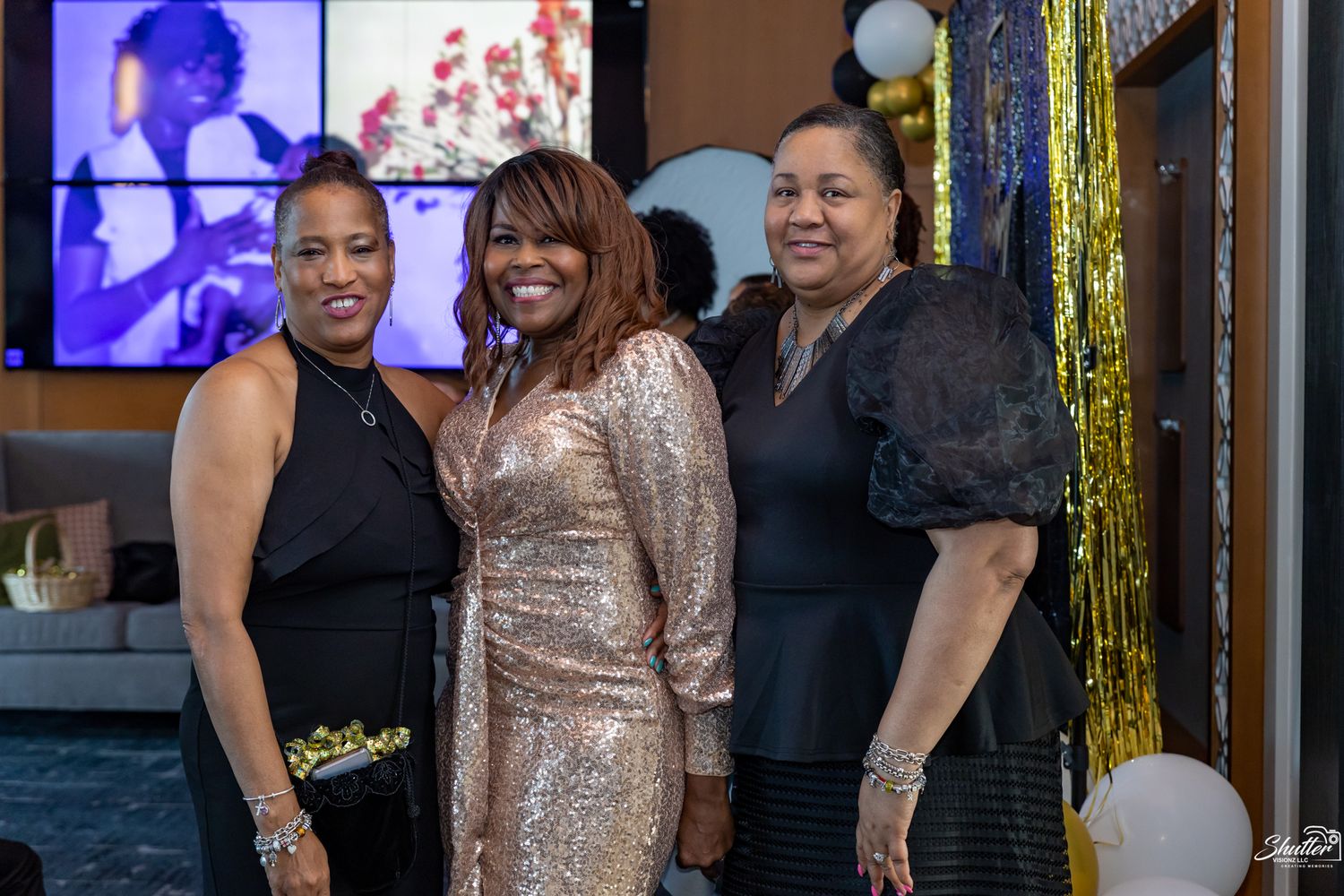 Three women smiling together at a celebration surrounded by gold decorations