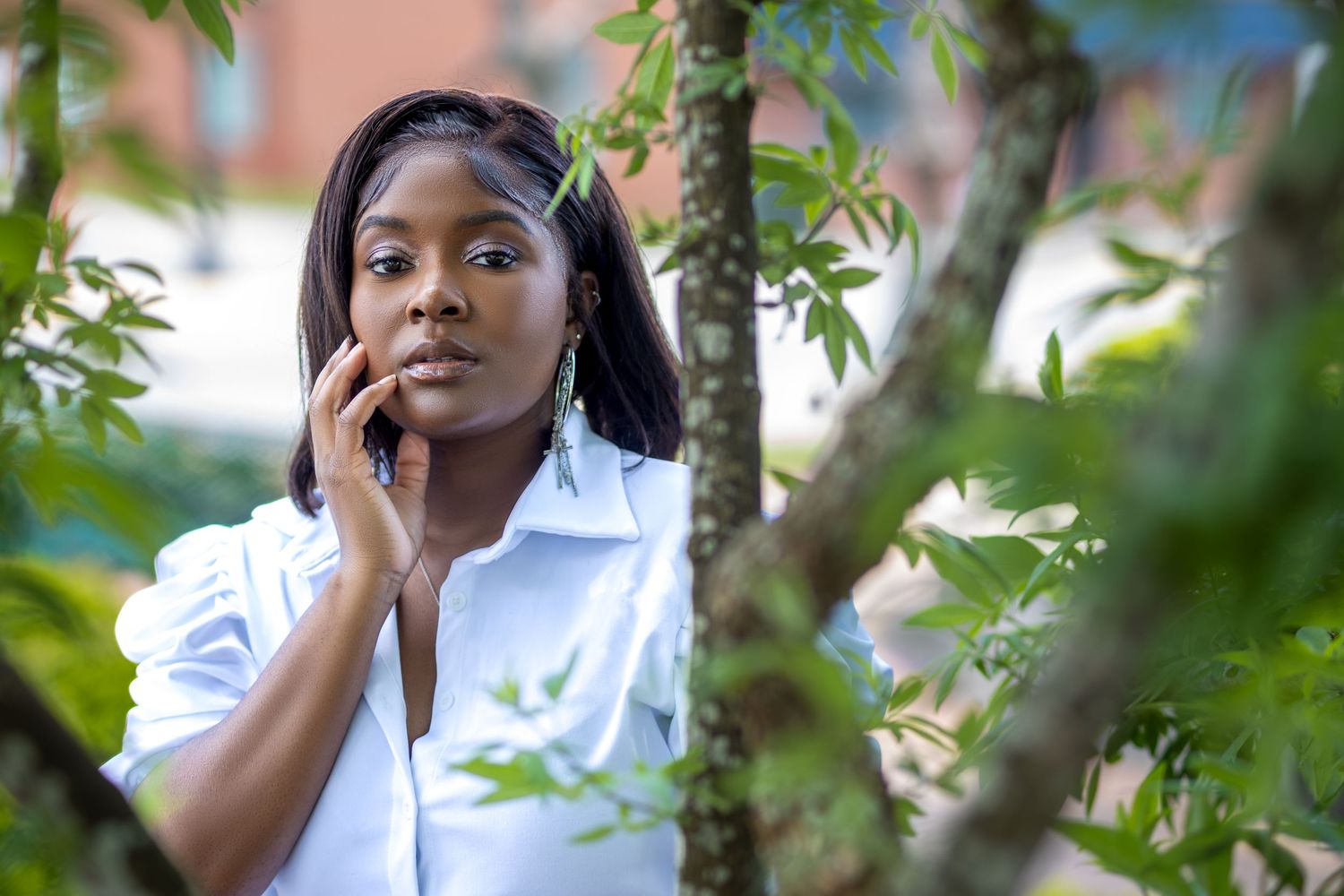 Woman in white shirt talks on phone while standing among tree branches outdoors.