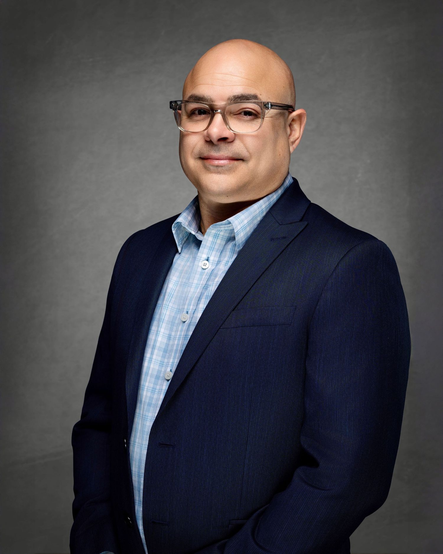 Professional headshot of a man wearing glasses, a navy blazer and light blue shirt