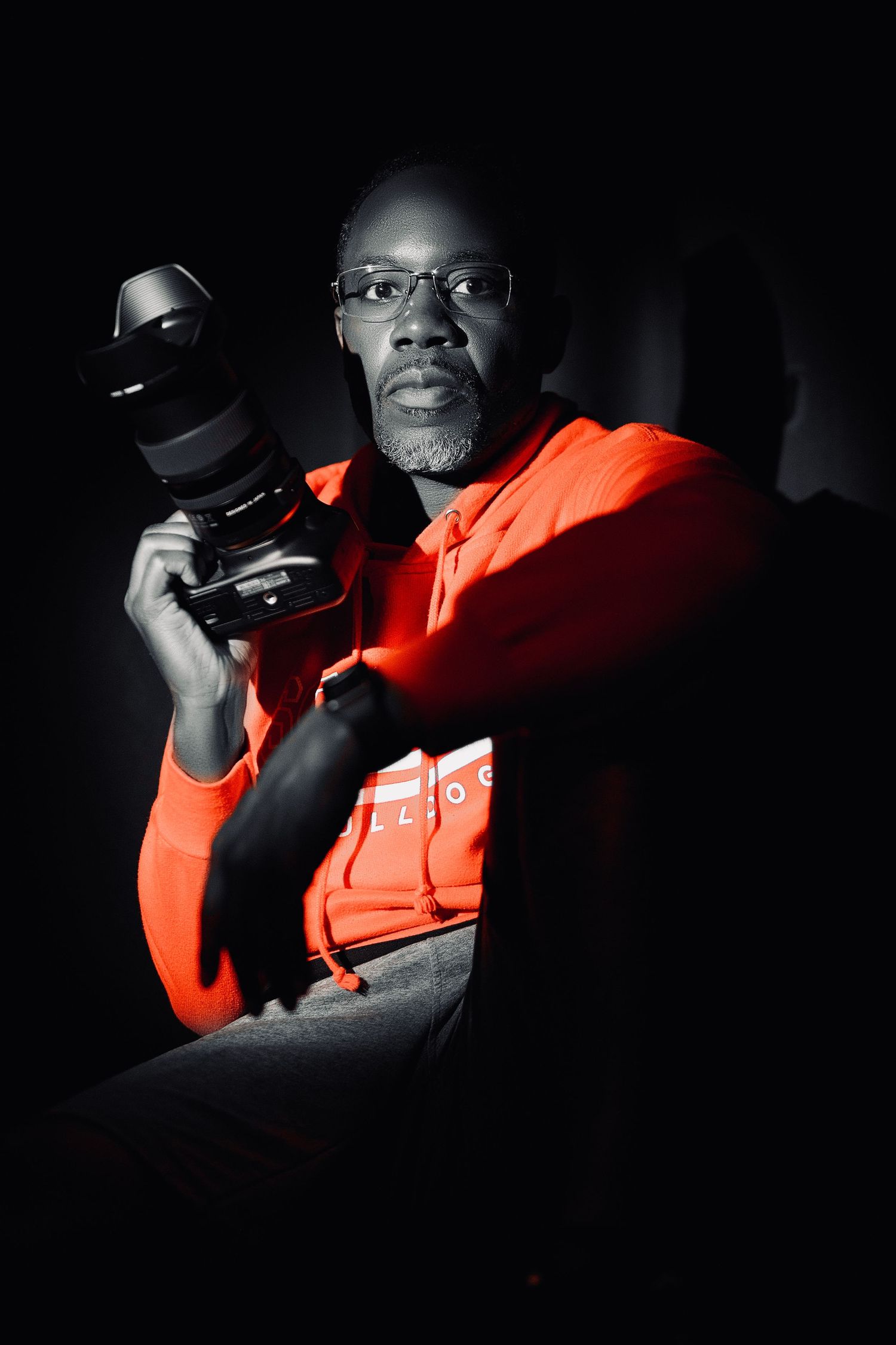Dramatic portrait of a photographer holding a professional camera while wearing a red hoodie